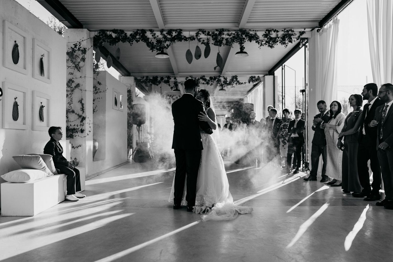 Black and white photo of bride and groom first dance surrounded by smoke and wedding guests.