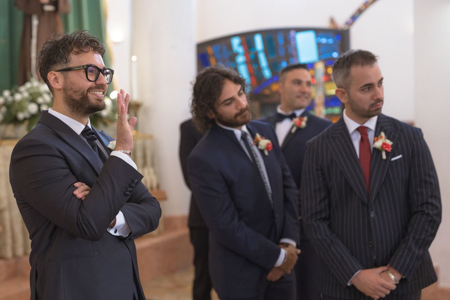 Three well-dressed groomsmen in suits standing inside a church during a wedding ceremony.