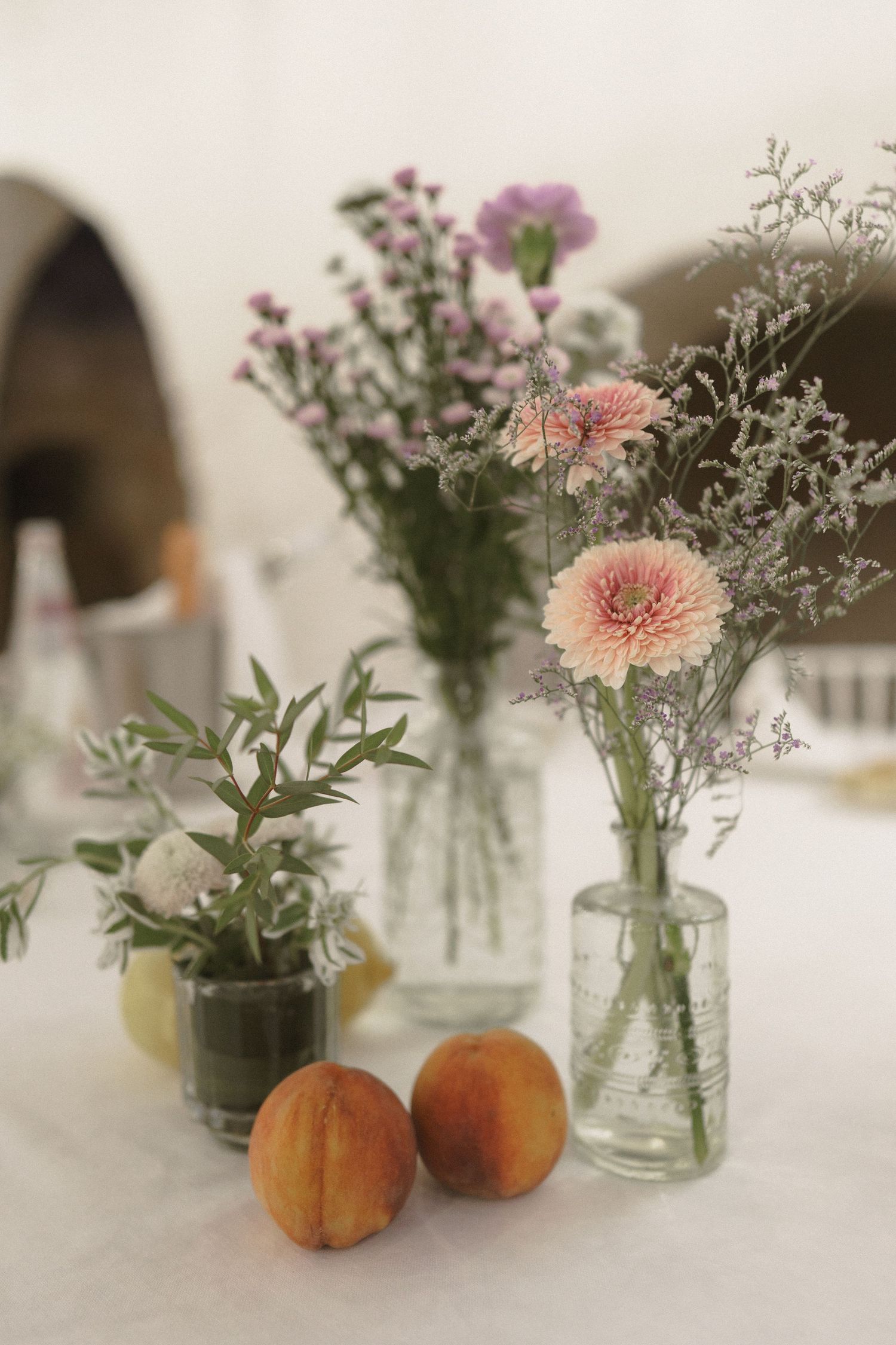 Fresh peach flowers in glass vases with delicate pink chrysanthemums and wildflowers on a white tablecloth.