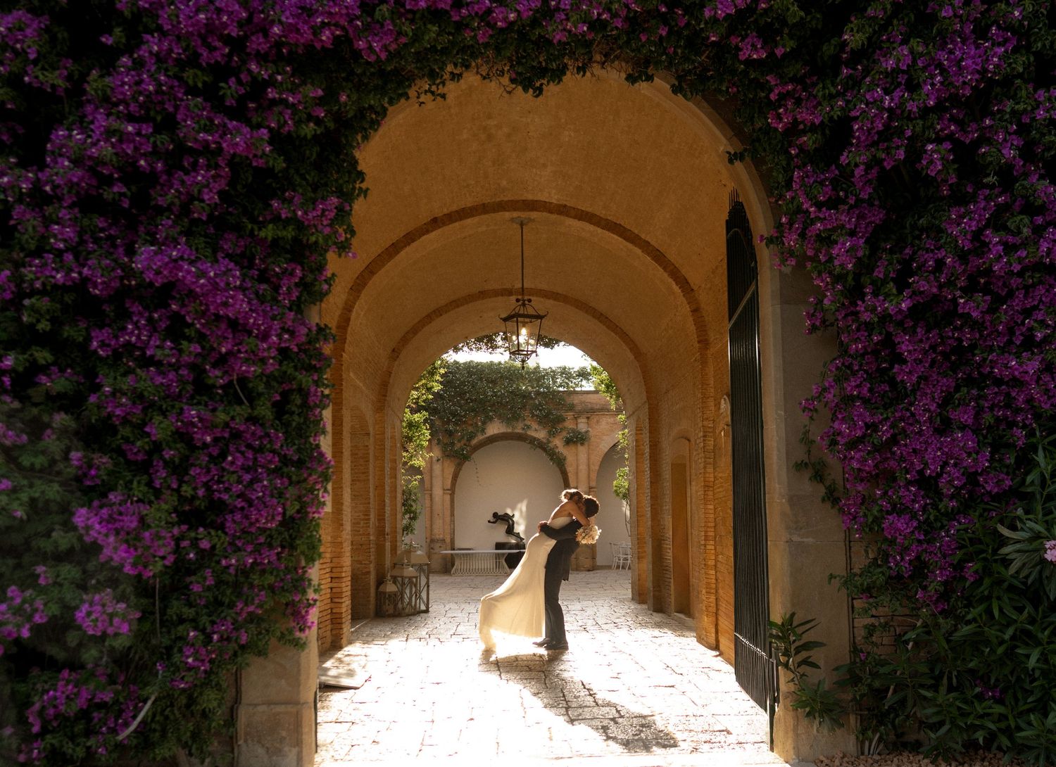 Romantic dance sequence under stone archways adorned with vibrant purple bougainvillea flowers.