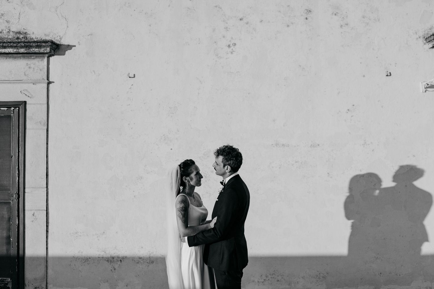 A romantic silhouette moment between newlyweds against a white wall.