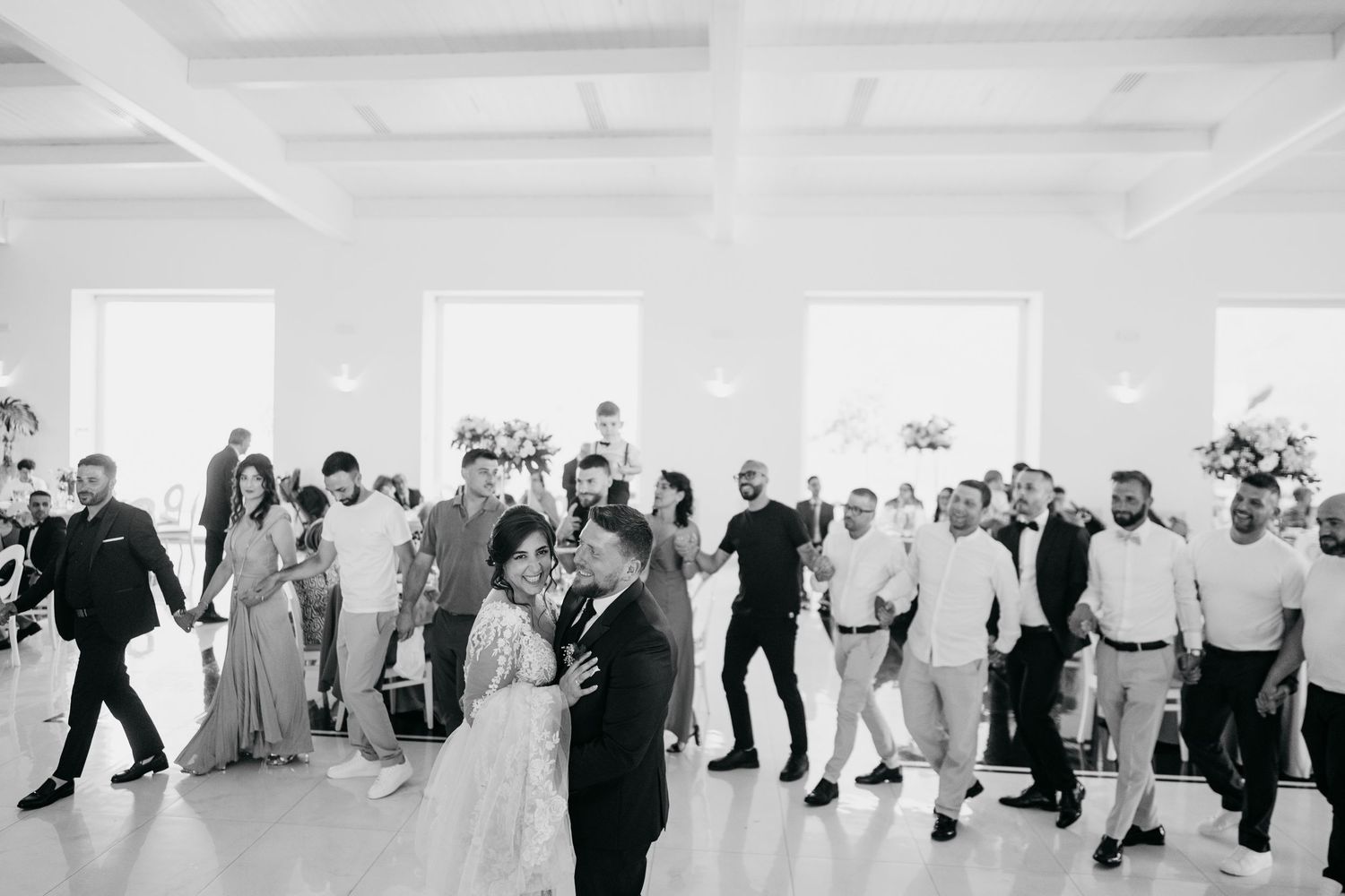 Panoramic view of wedding guests dancing and celebrating in a bright reception hall.