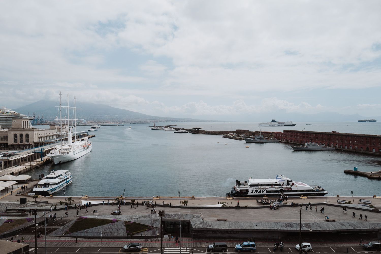 Aerial view of a marina with boats docked at the harbor and ships visible in the misty waters beyond.