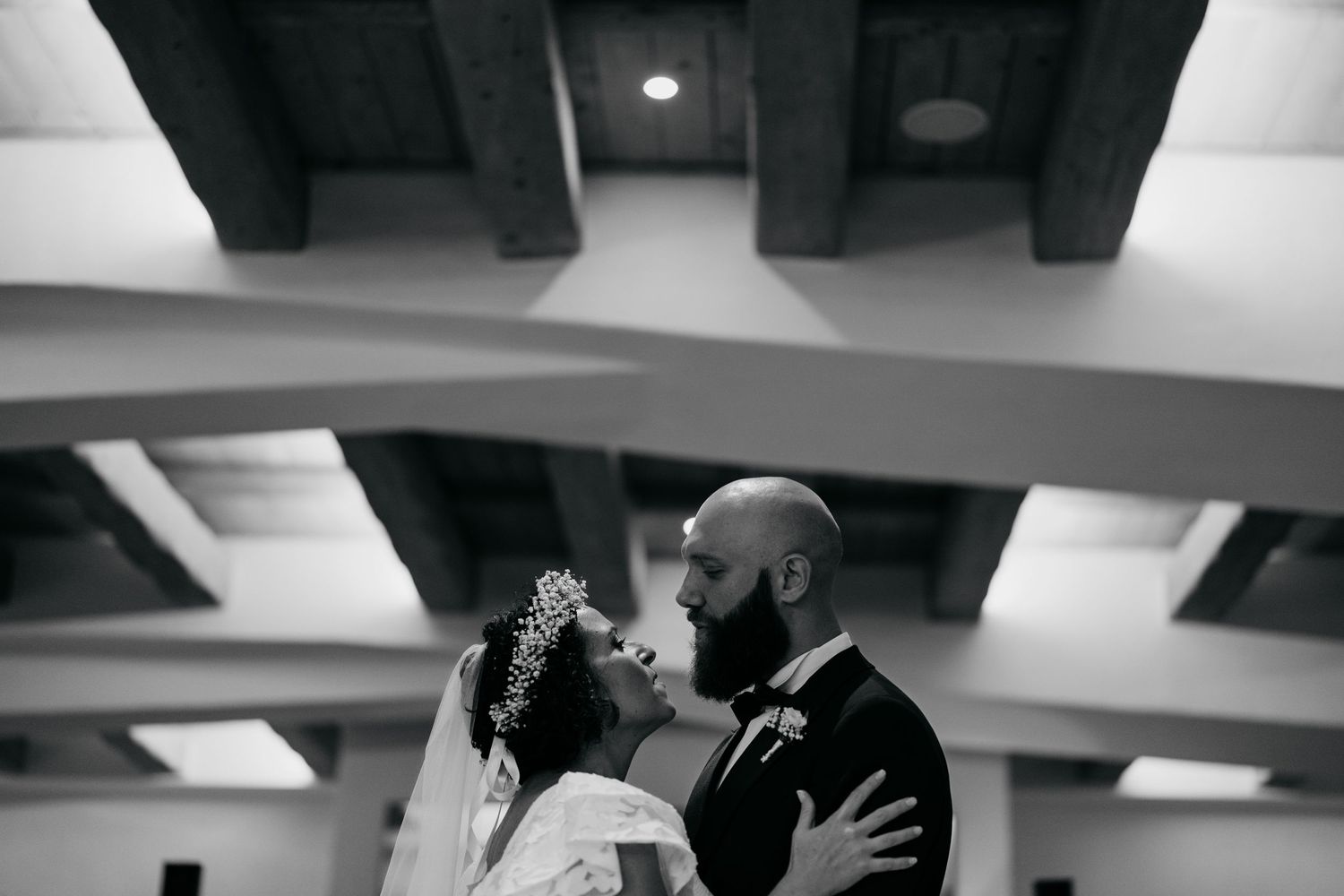 An intimate black and white wedding dance moment between newlyweds in an indoor reception venue with exposed beams.
