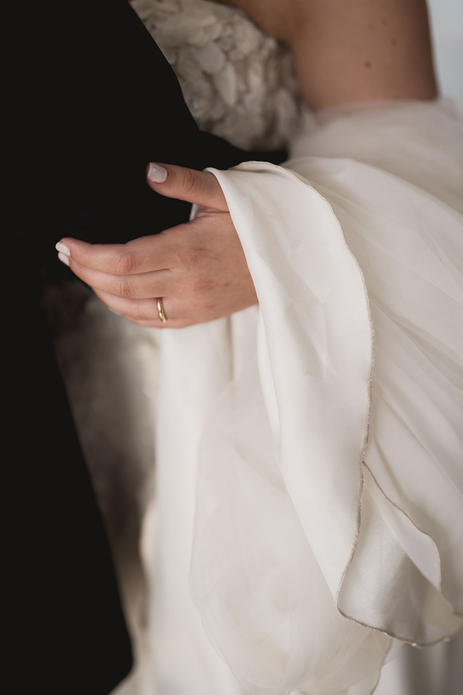 Detail shot of a bride's hand with wedding ring against white dress fabric.