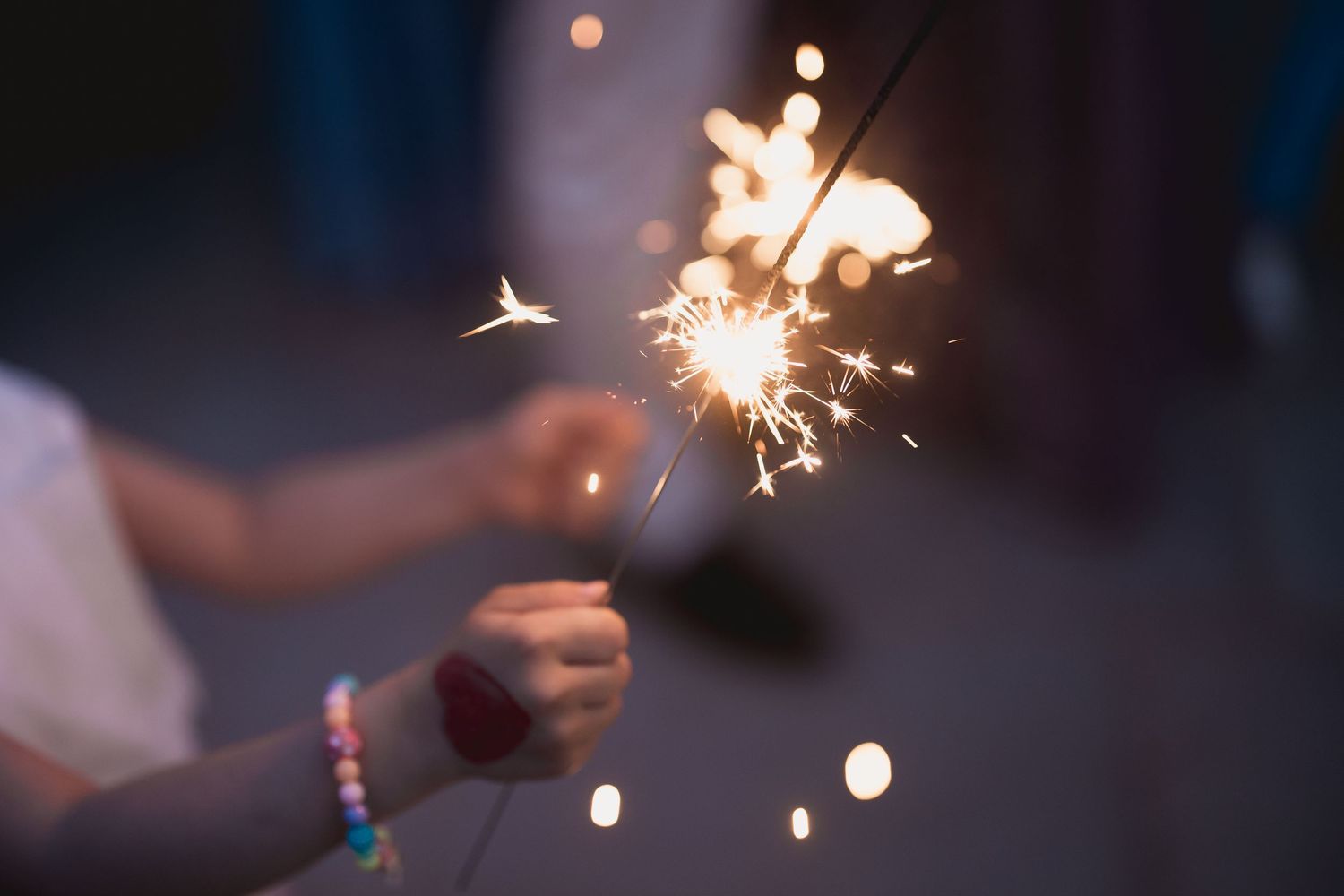 Hand holding lit sparkler with bokeh lights in dark background.