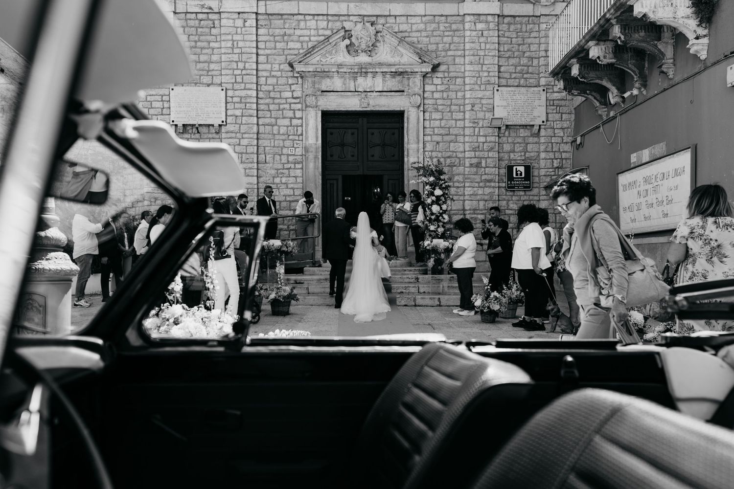 Black and white view of church entrance through car windshield during wedding.