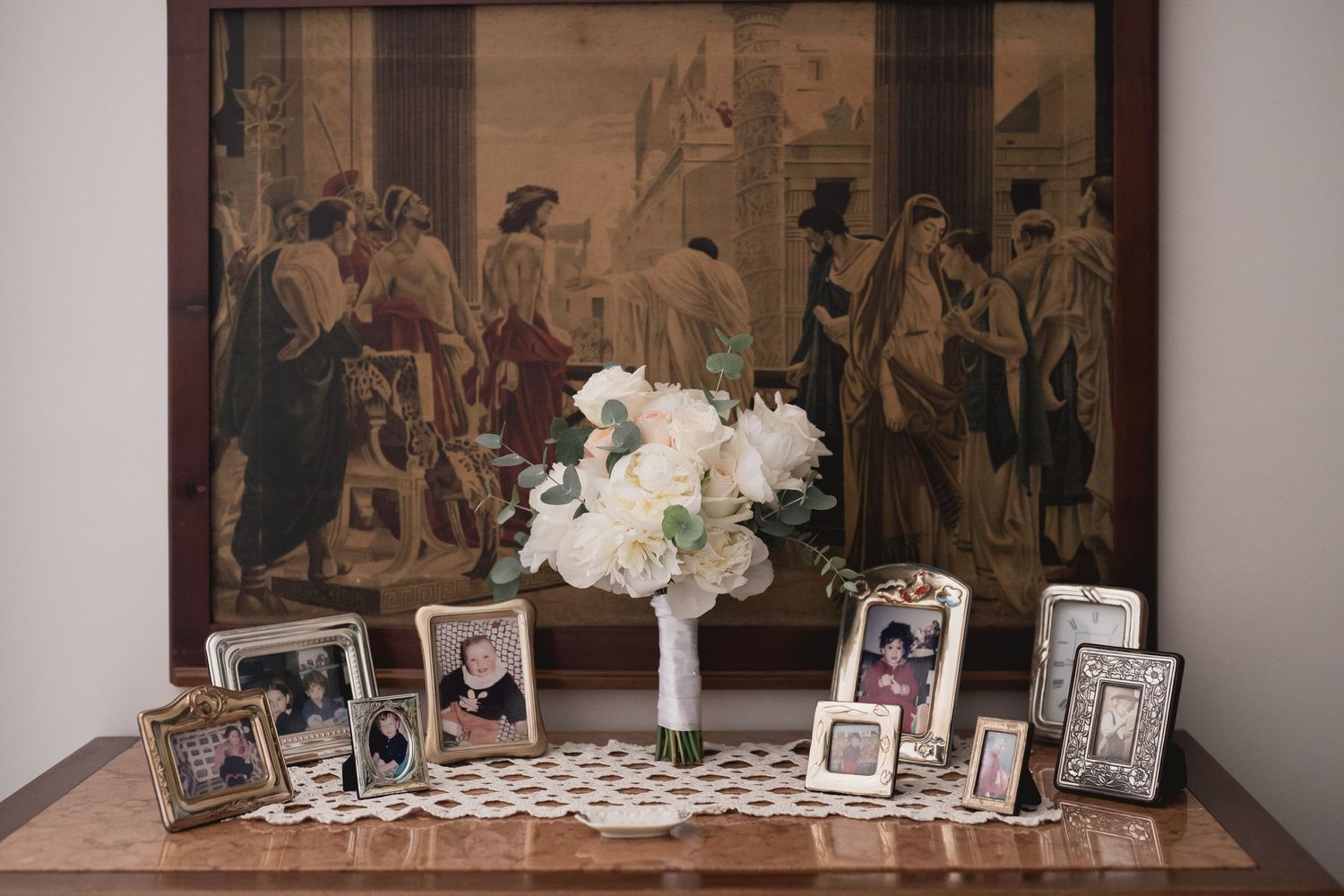 A table display with vintage artwork, white flowers and framed family photographs.