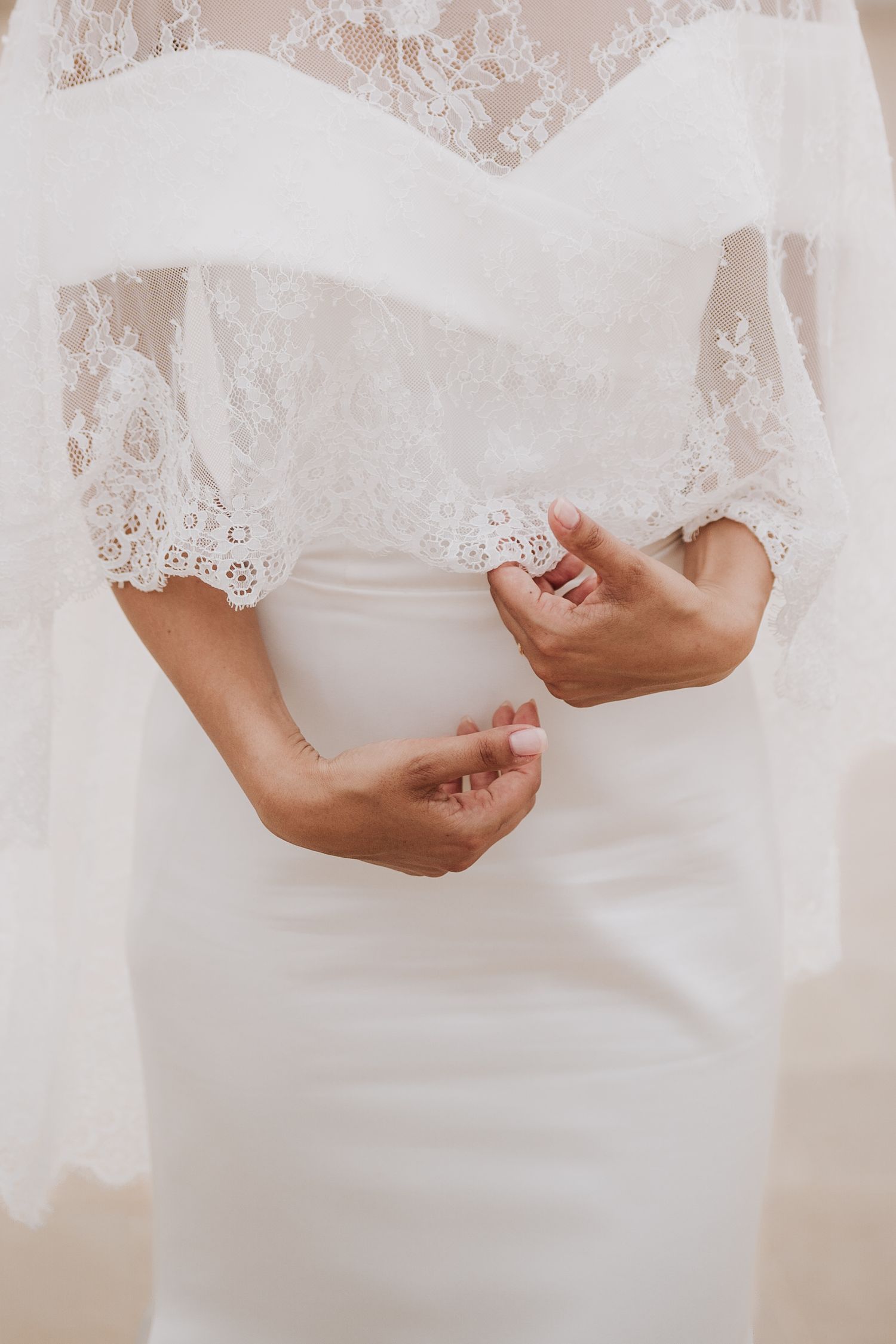 Close-up detail of delicate lace wedding dress with hands adjusting the fabric.