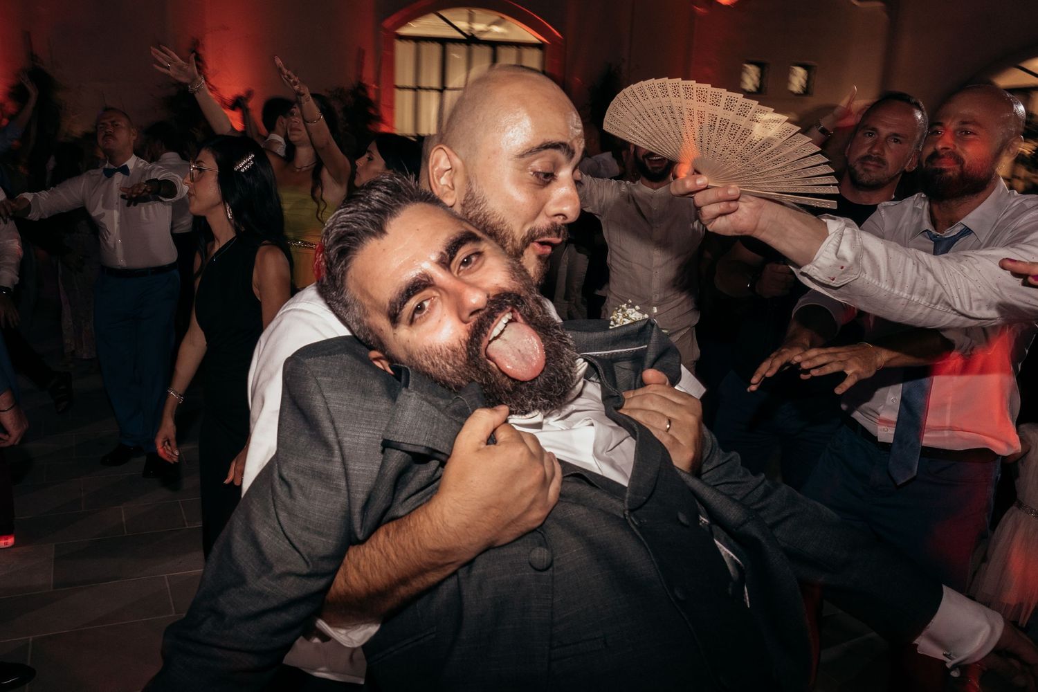 Energetic partygoers engage in playful celebration with exuberant expressions at a dimly lit reception.