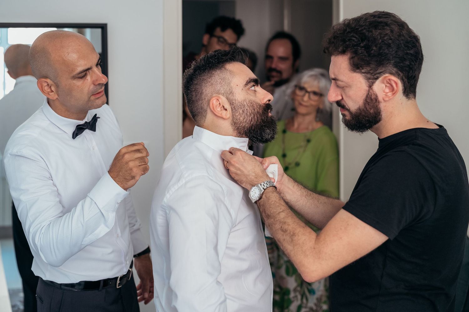 A group helping with formal attire preparations in a white room with a mirror.
