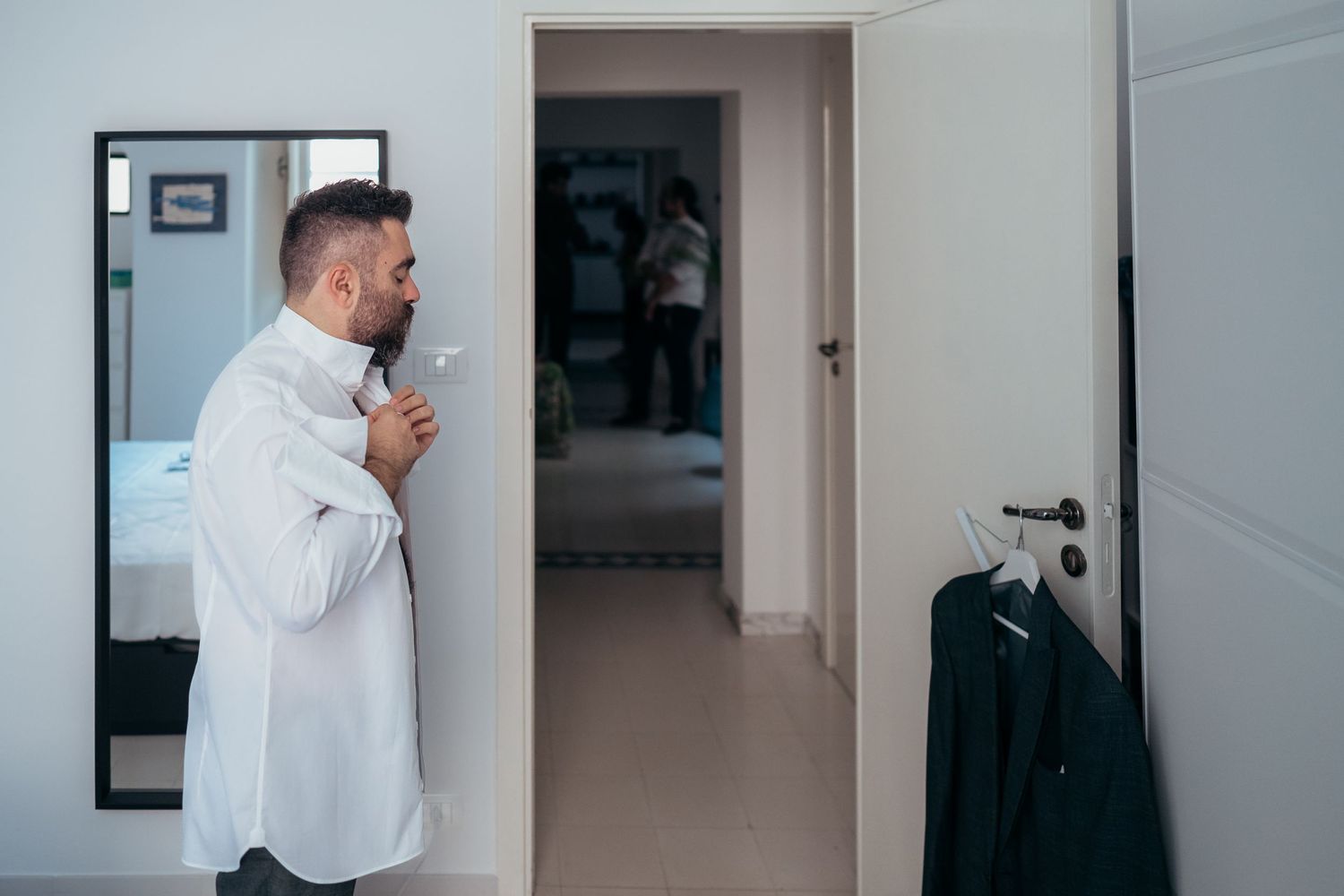 Person buttoning up white dress shirt in hallway.
