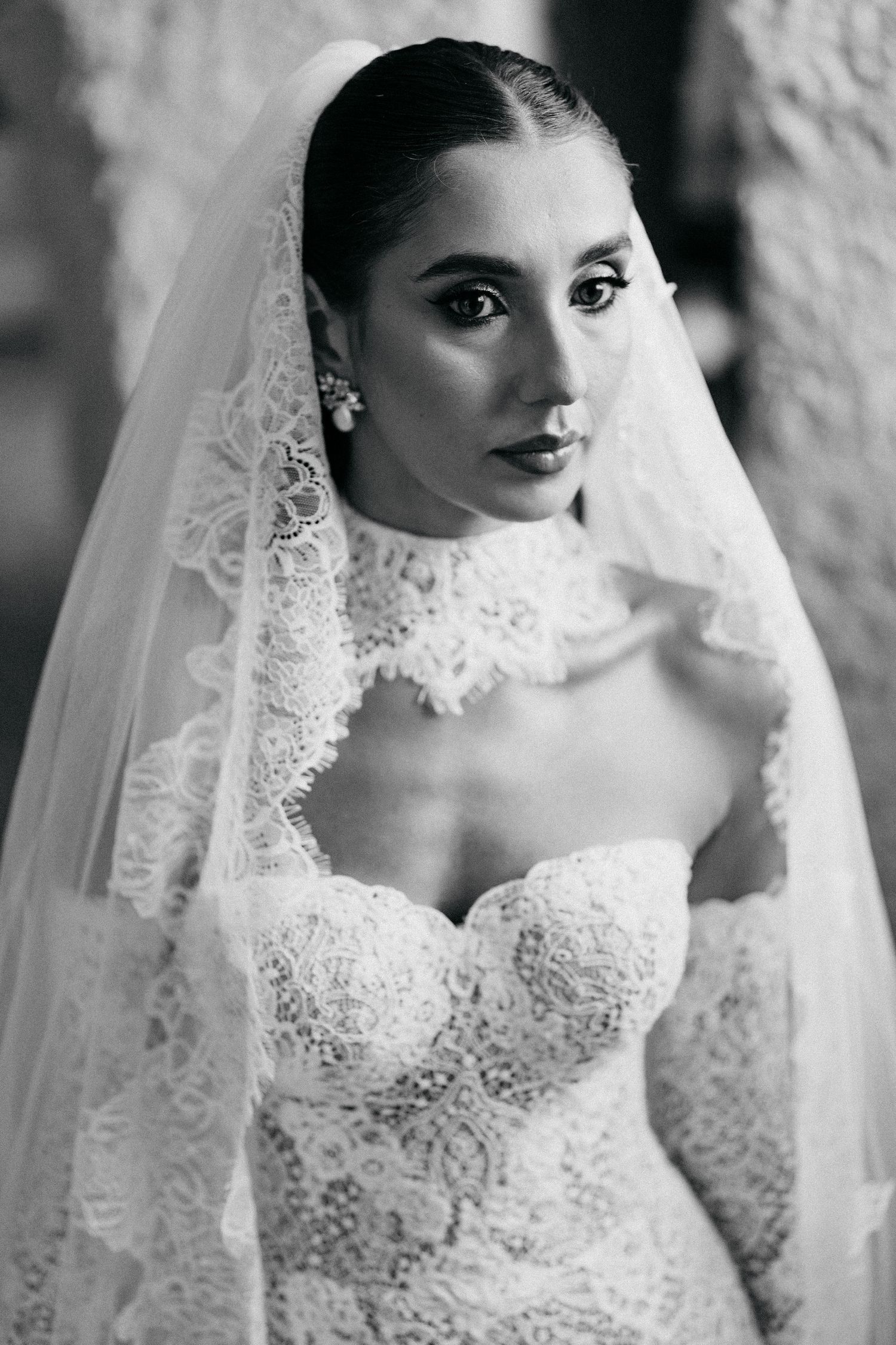 Black and white portrait of a bride in a lace-trimmed veil and strapless lace gown with a high lace choker collar.
