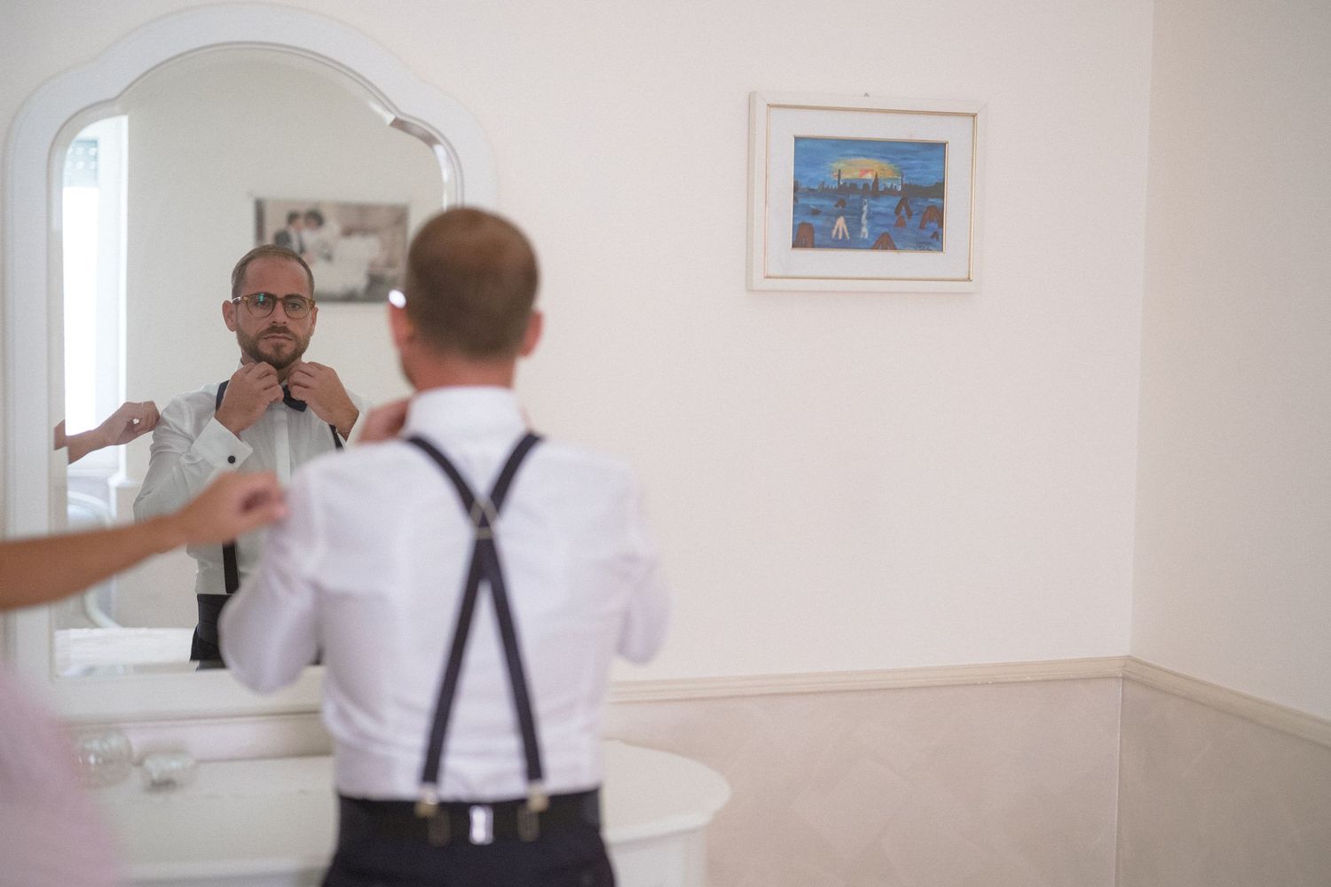 Two men in business attire perform a comedic mirror reflection scene in front of a white wall.