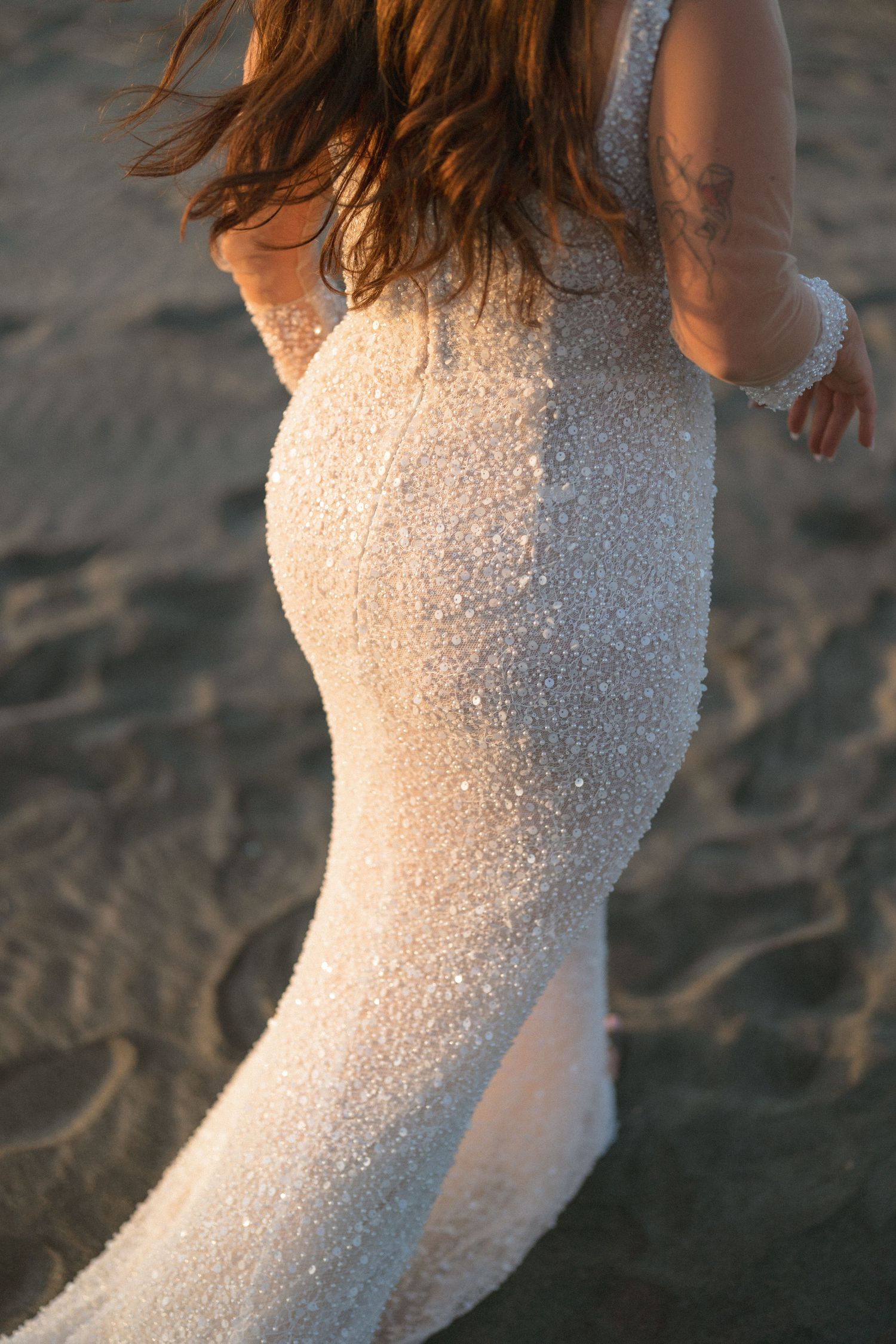 Sparkling sequined wedding dress detail captured at sunset on beach sand.