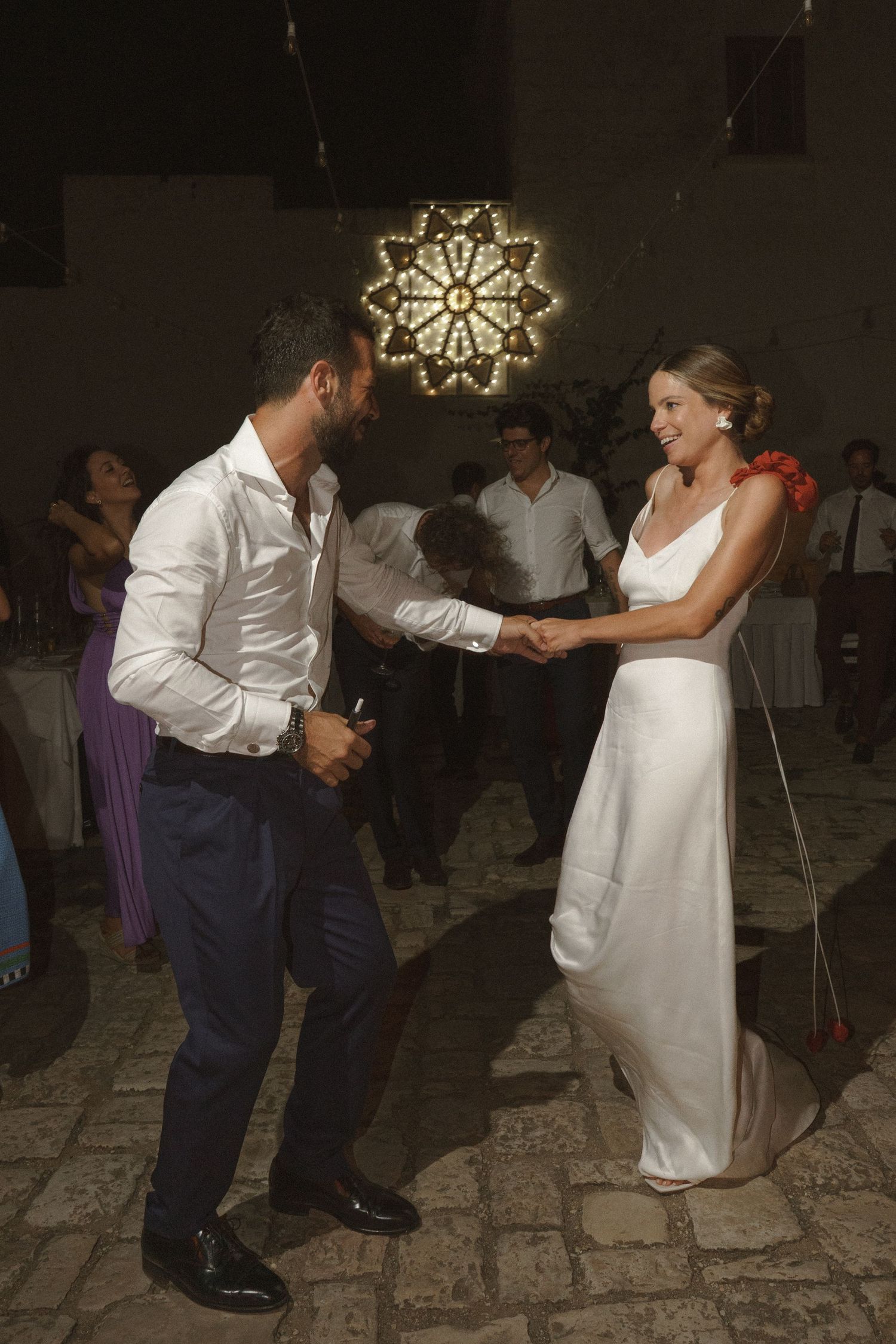 Wedding couple dancing under an illuminated snowflake decoration on a stone floor.