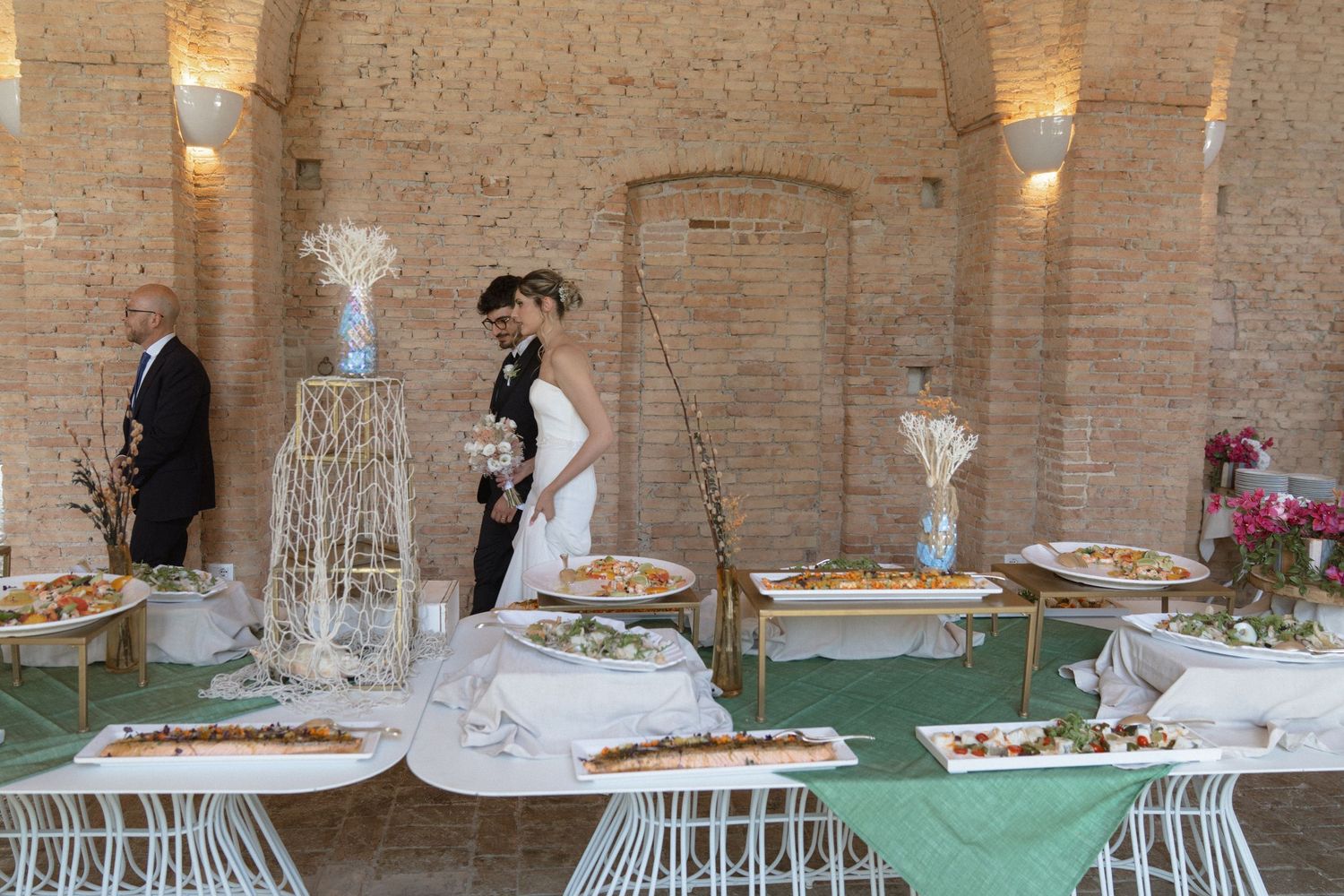 Elegant wedding reception tables decorated with white linens and floral centerpieces in a rustic stone-walled venue.