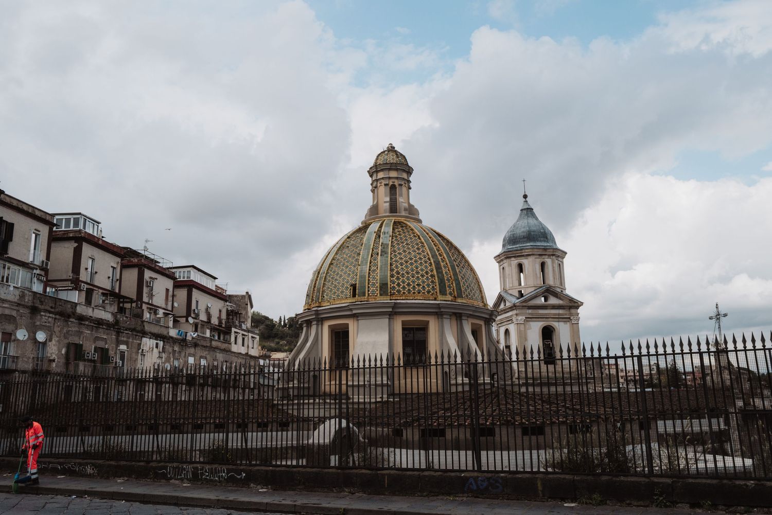 Golden domed church with ornate architecture behind iron fence in Naples cityscape.