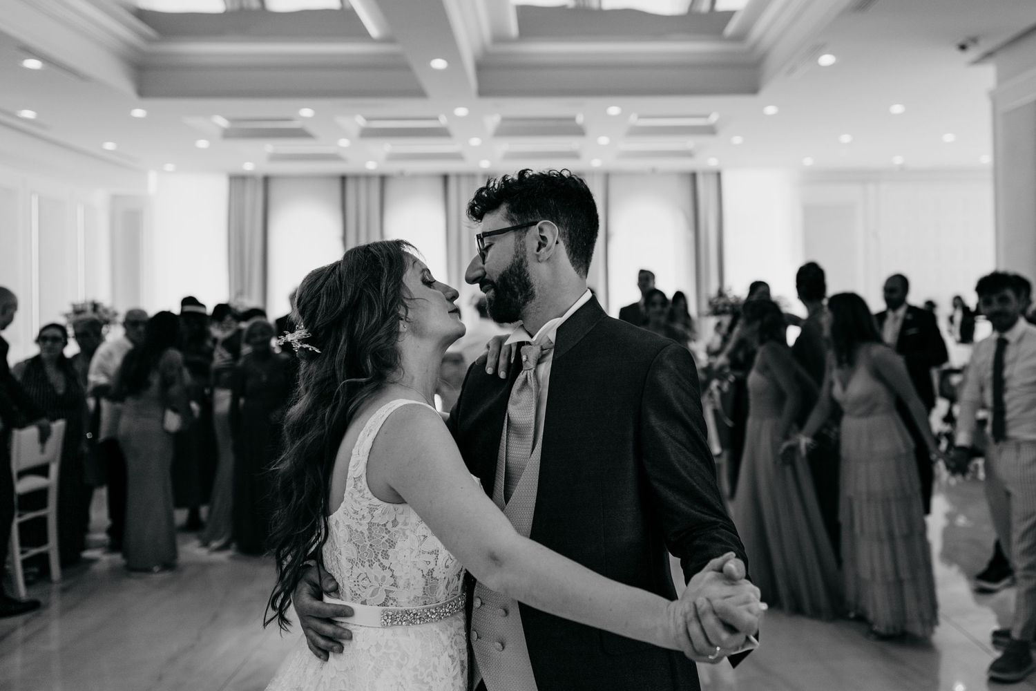 Wedding couple shares their first dance in an elegant ballroom surrounded by guests.