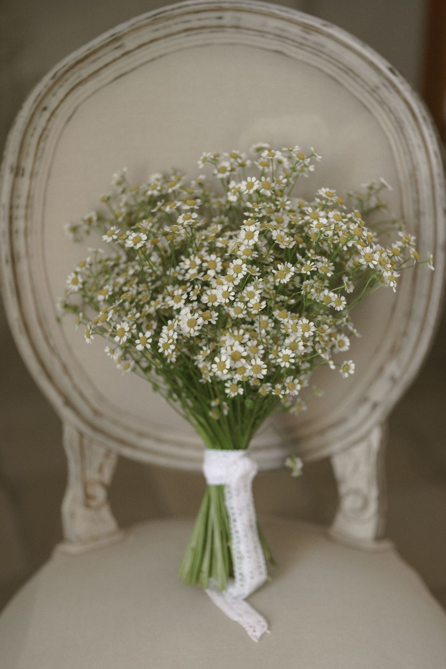 A delicate bouquet of white baby's breath flowers tied with lace ribbon sits on an antique chair.