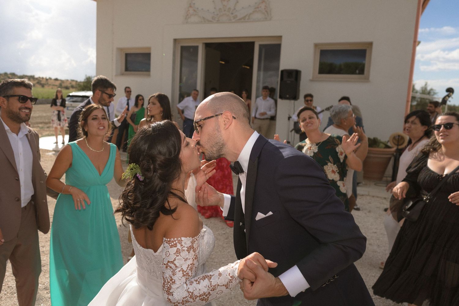 Wedding celebration with guests mingling outside white building.