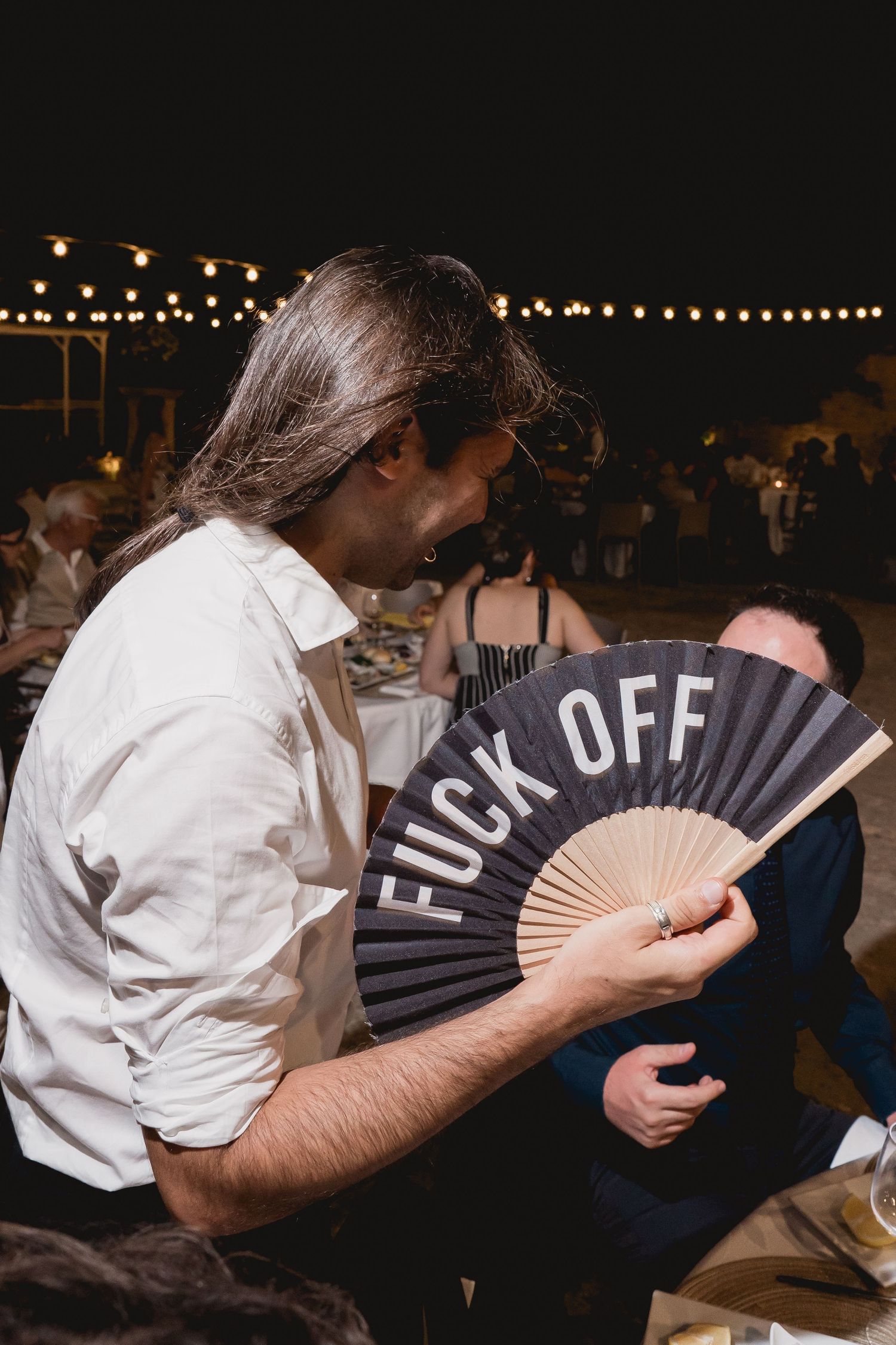Wedding guest holds up a decorative black hand fan with 