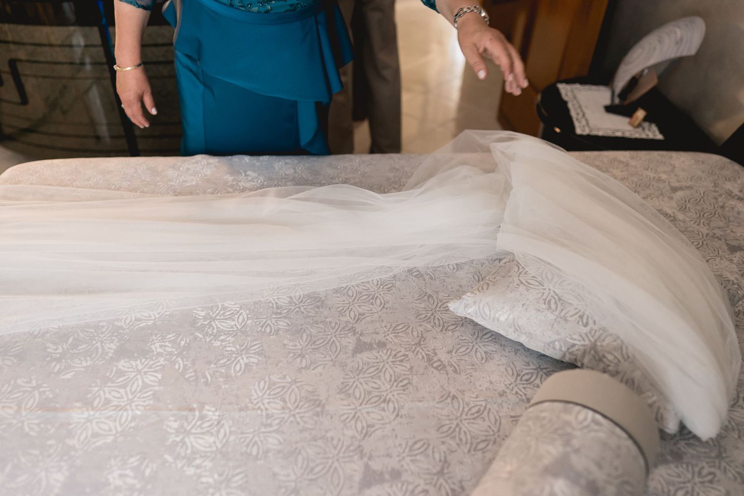 Close-up detail shot of a white wedding dress laid out on a bed.