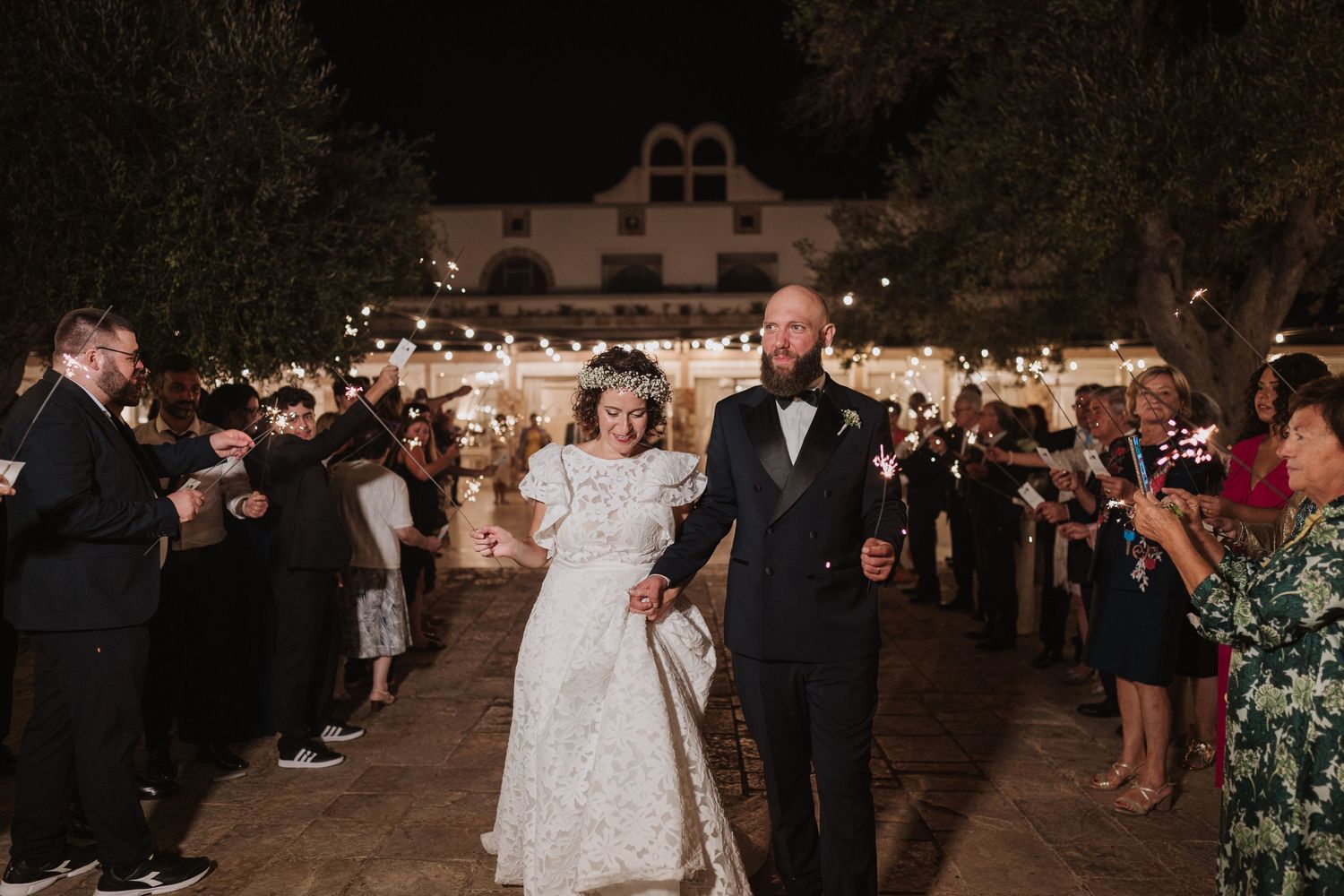 Wedding celebration with guests holding sparklers during a nighttime outdoor exit.