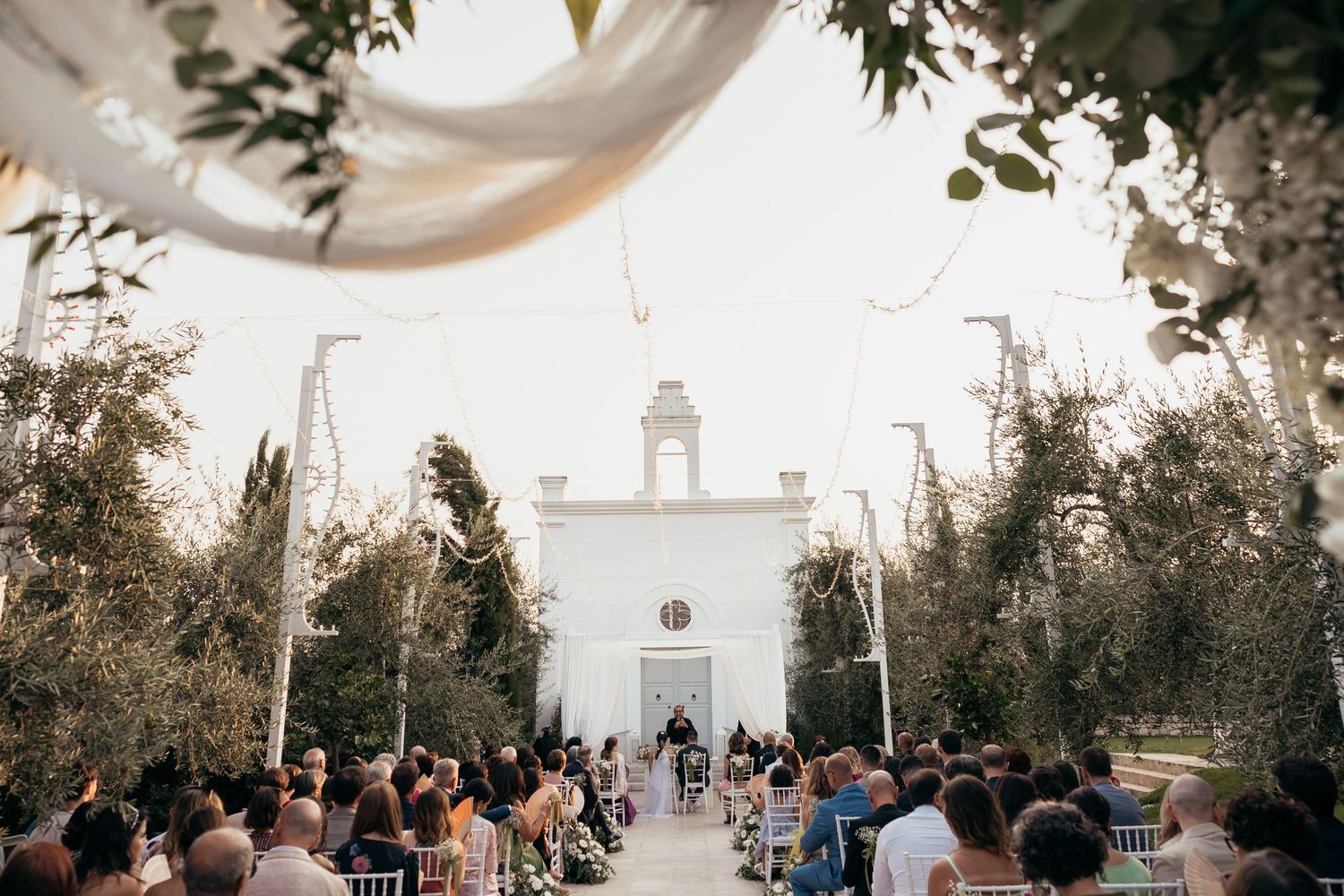 Outdoor wedding ceremony setup with white chapel and floral arch decorations.