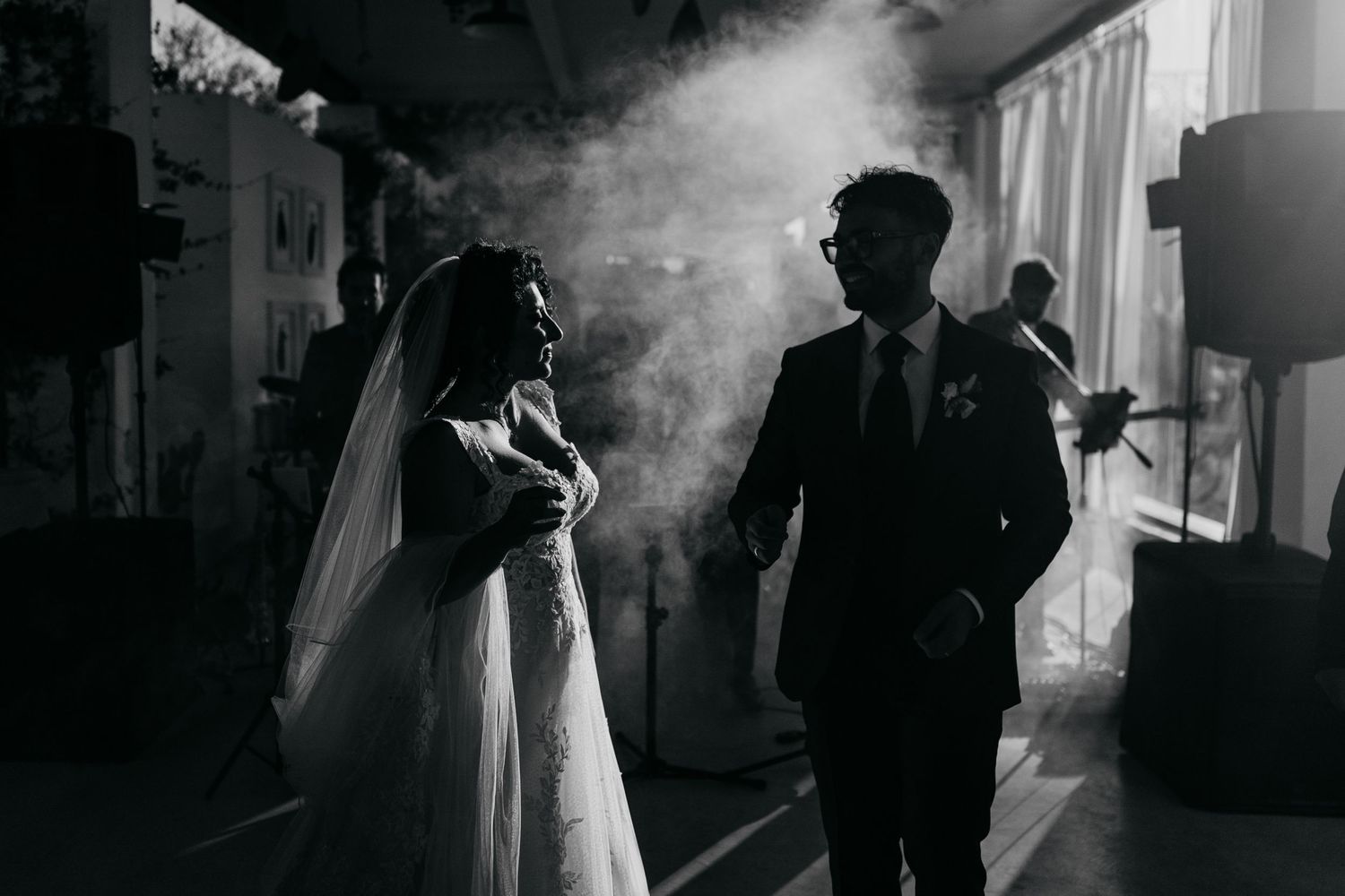 Dramatic black and white silhouette of bride and groom standing in atmospheric smoke at wedding.