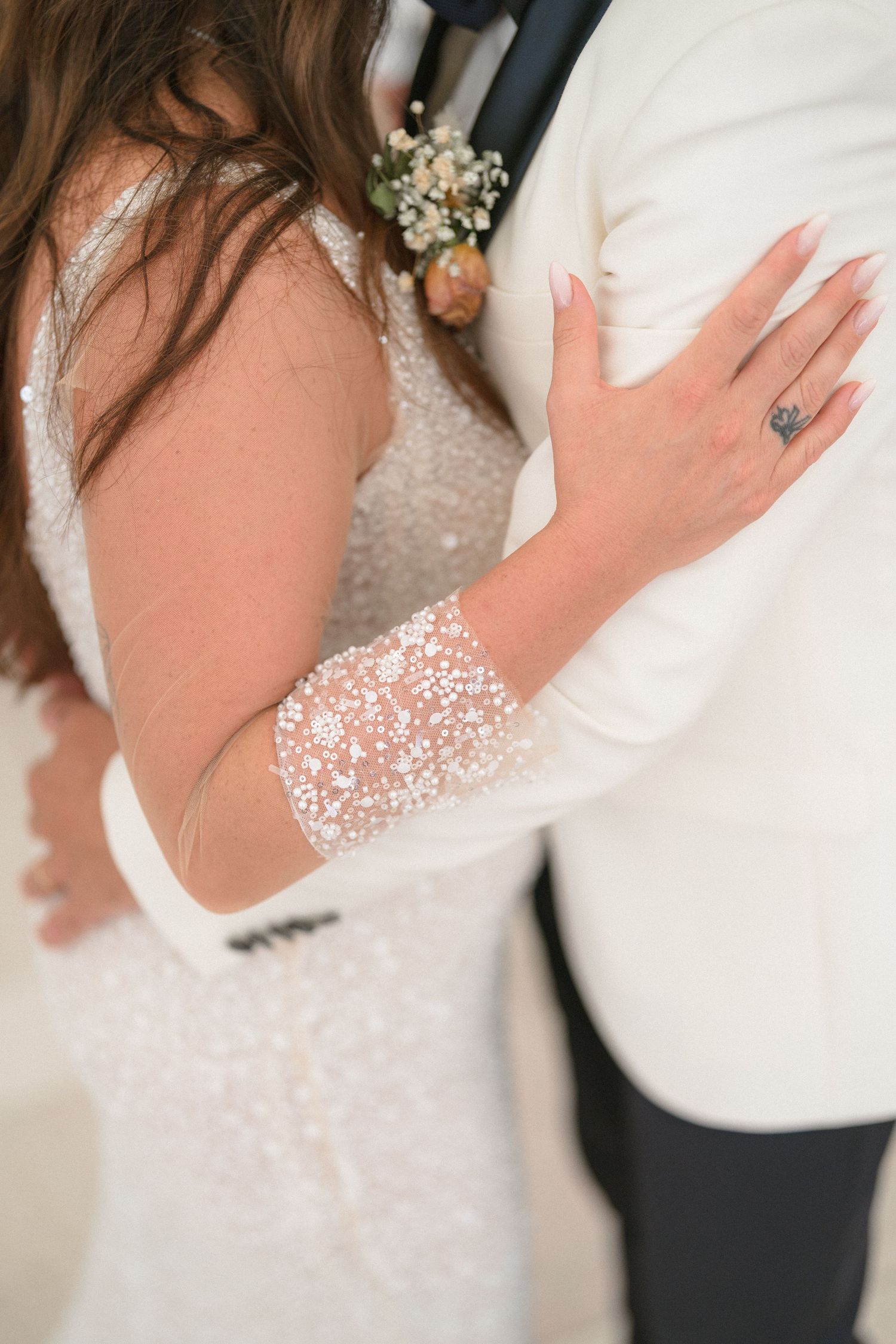 Detail shot of bride's sparkly sleeve and engagement ring against groom's white jacket.