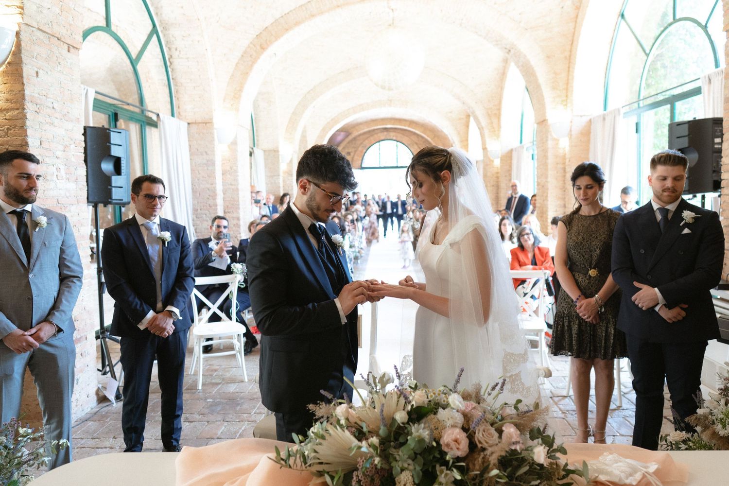 Wedding celebration in a bright white arched venue with elegant decor and floral arrangements.