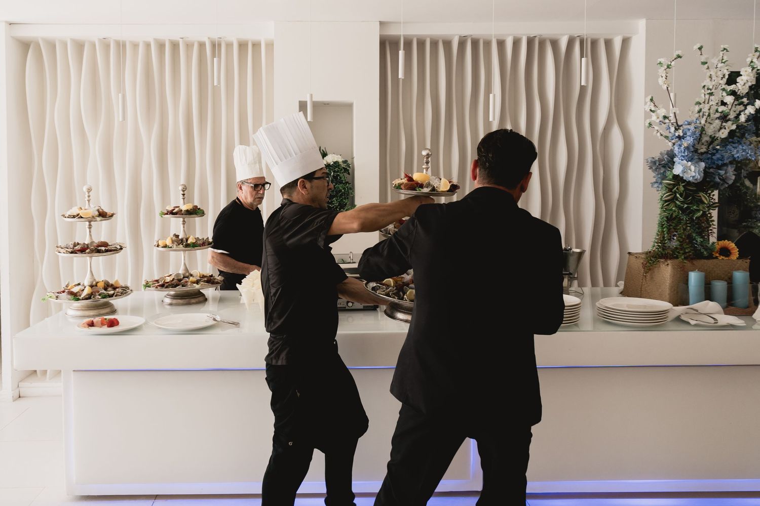 Two chefs in black uniforms preparing food at an elegant catering display.