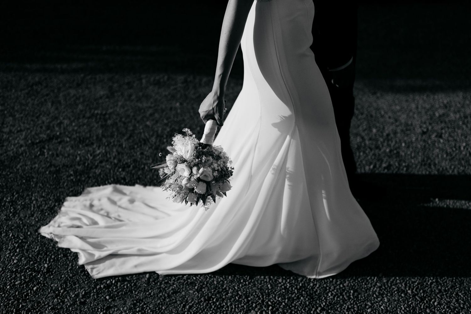 White wedding dress train flows elegantly across dark ground in dramatic lighting.
