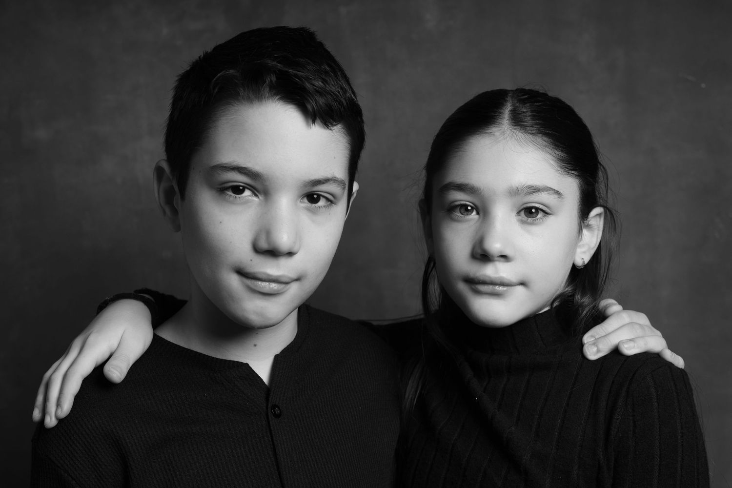 Black and white portrait of two young children wearing black turtlenecks in a studio setting.