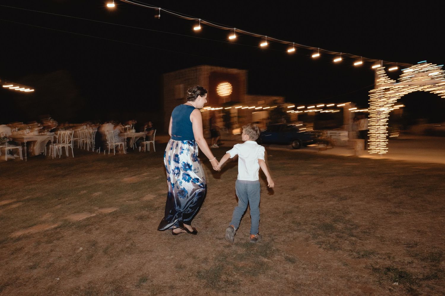 A nighttime dance under string lights at an outdoor venue with a rustic stone arch in the background.