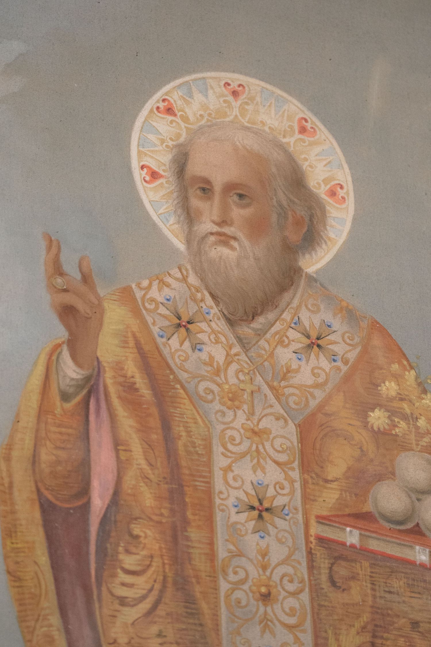 Religious artwork depicting a saint in ornate golden robes with a decorative halo against a gray background.