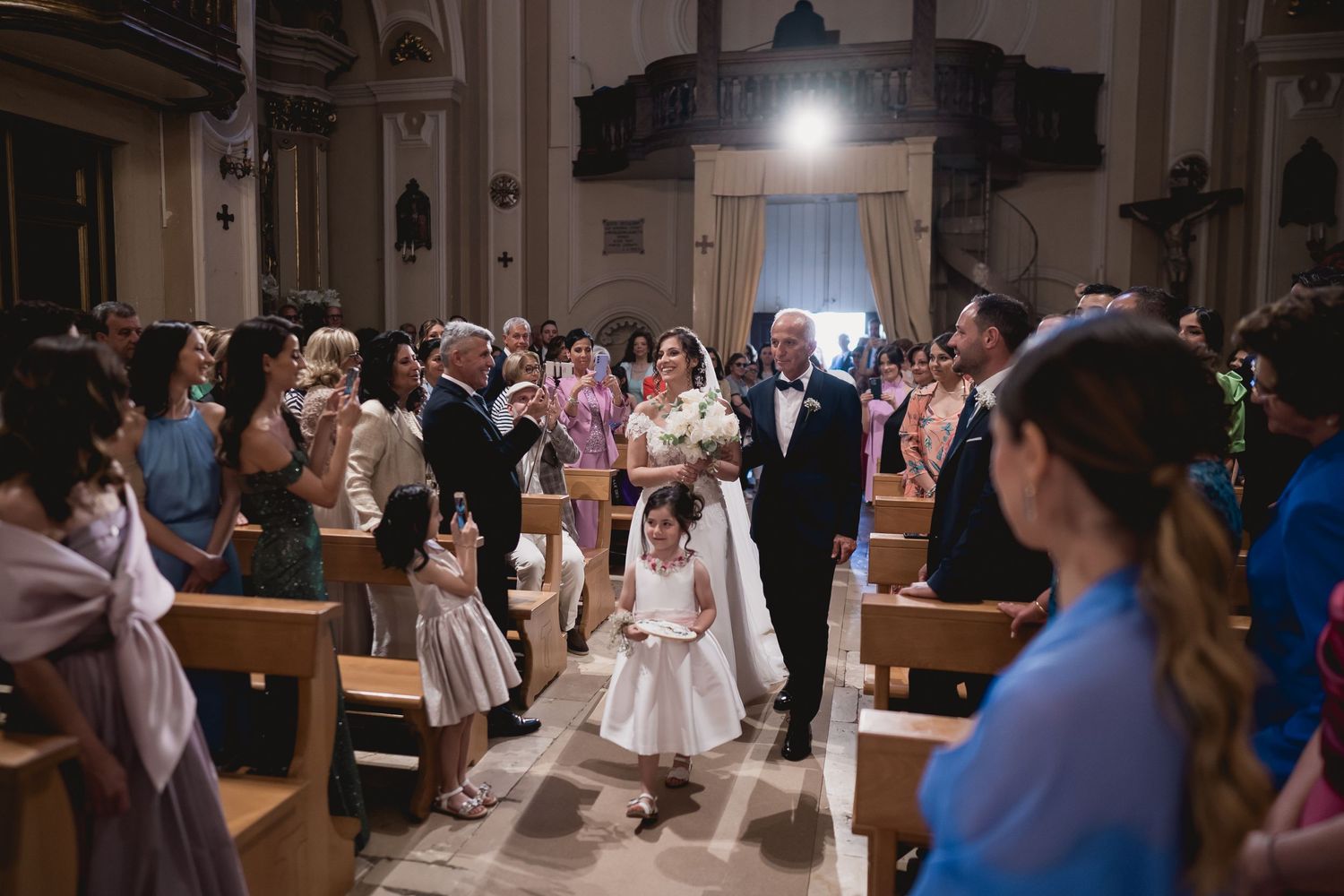 Wedding ceremony processional in church aisle with guests watching.