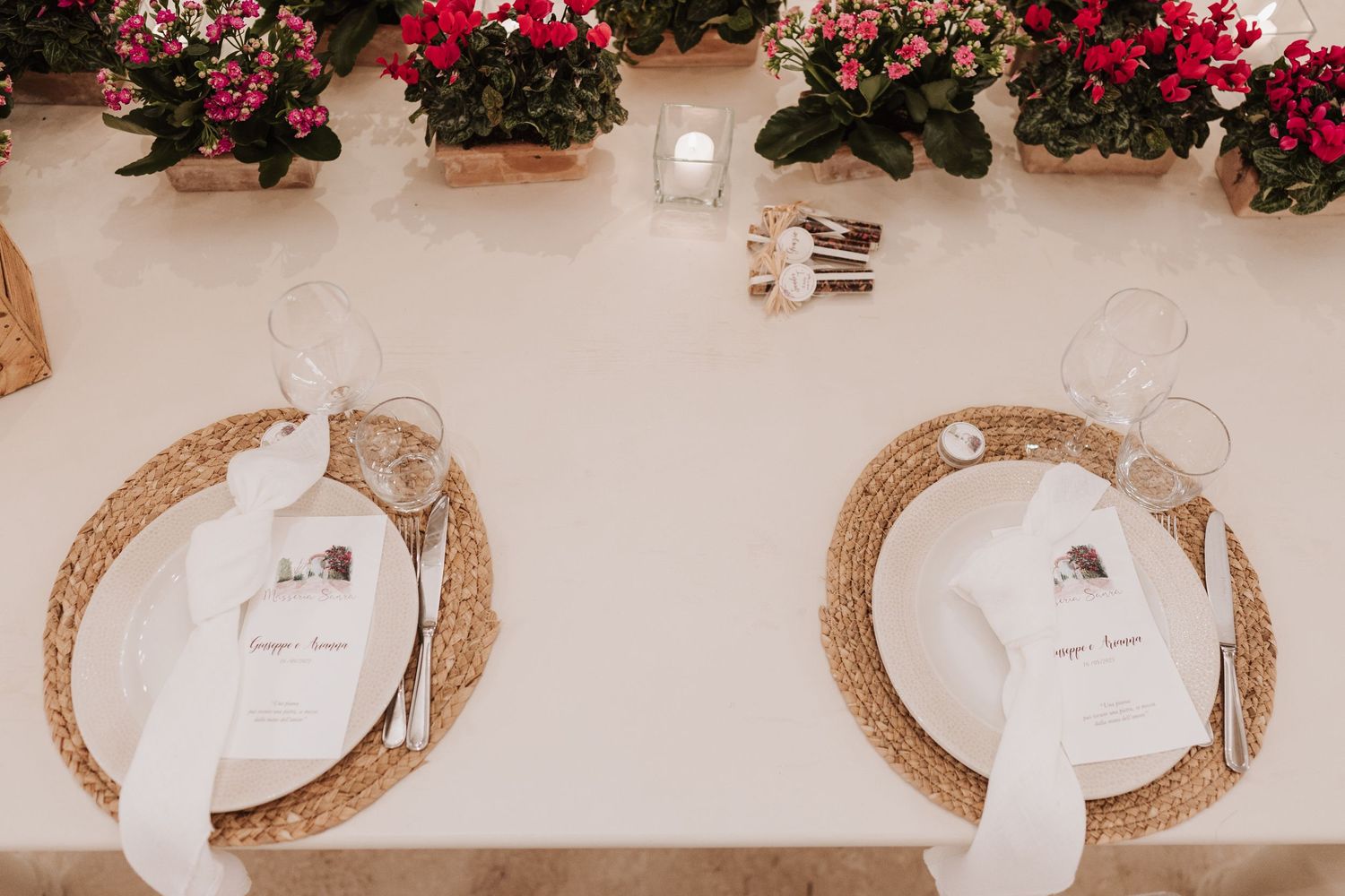 Wedding place settings with white plates on woven chargers and pink flowers as decoration.