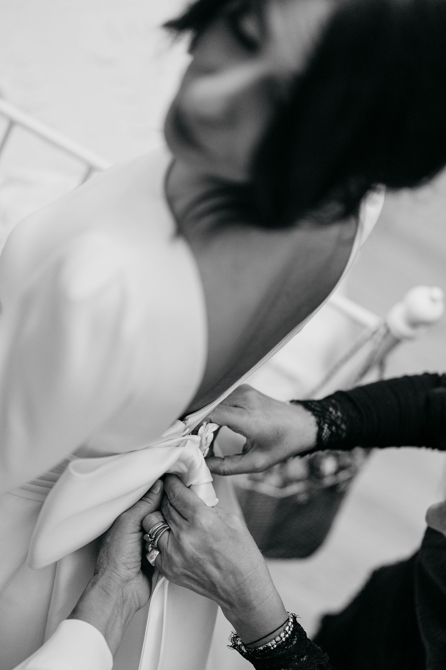 Black and white photo of hands fastening buttons on a white wedding dress.