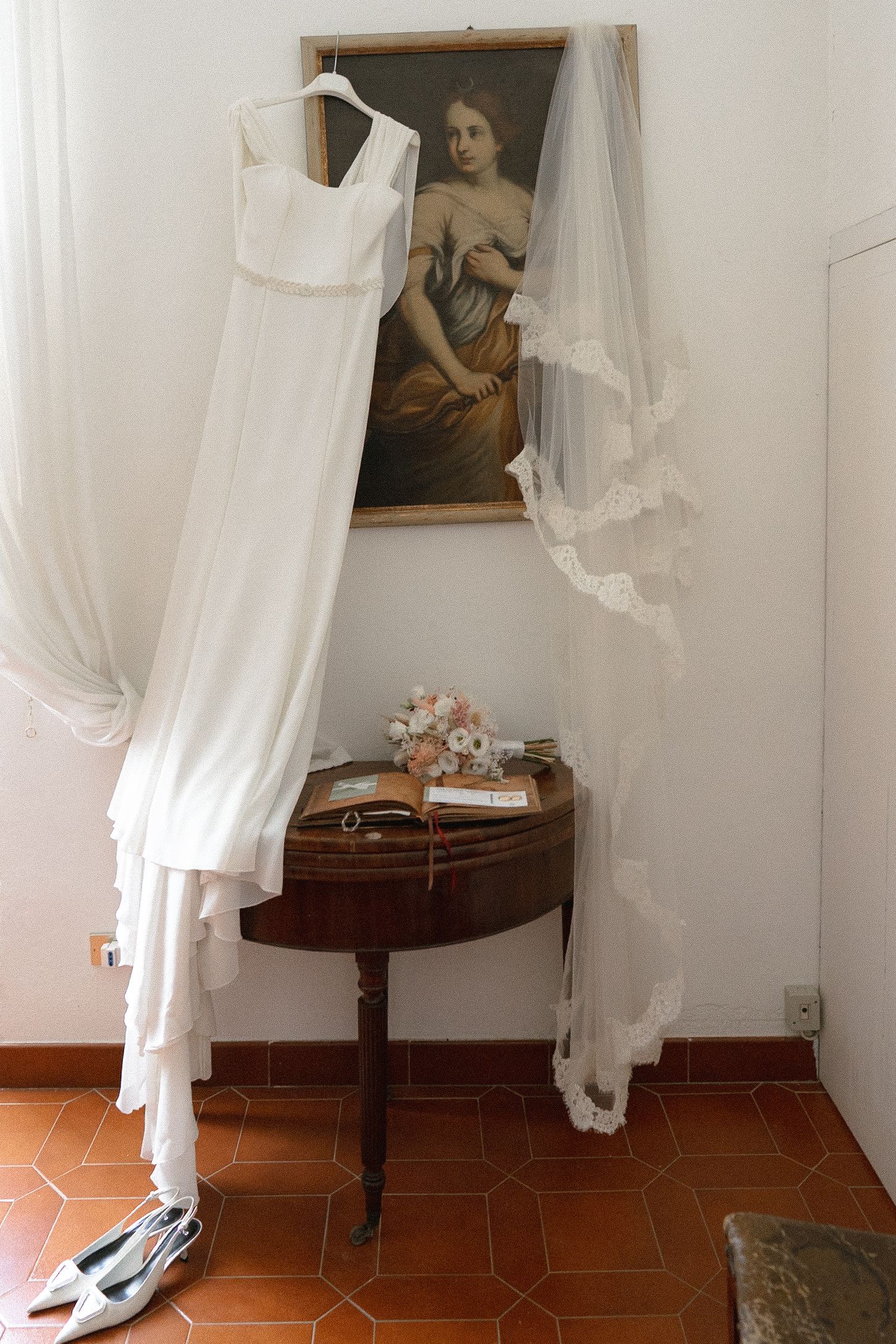 White wedding dress displayed in a minimalist room with terracotta flooring and antique wooden furniture.
