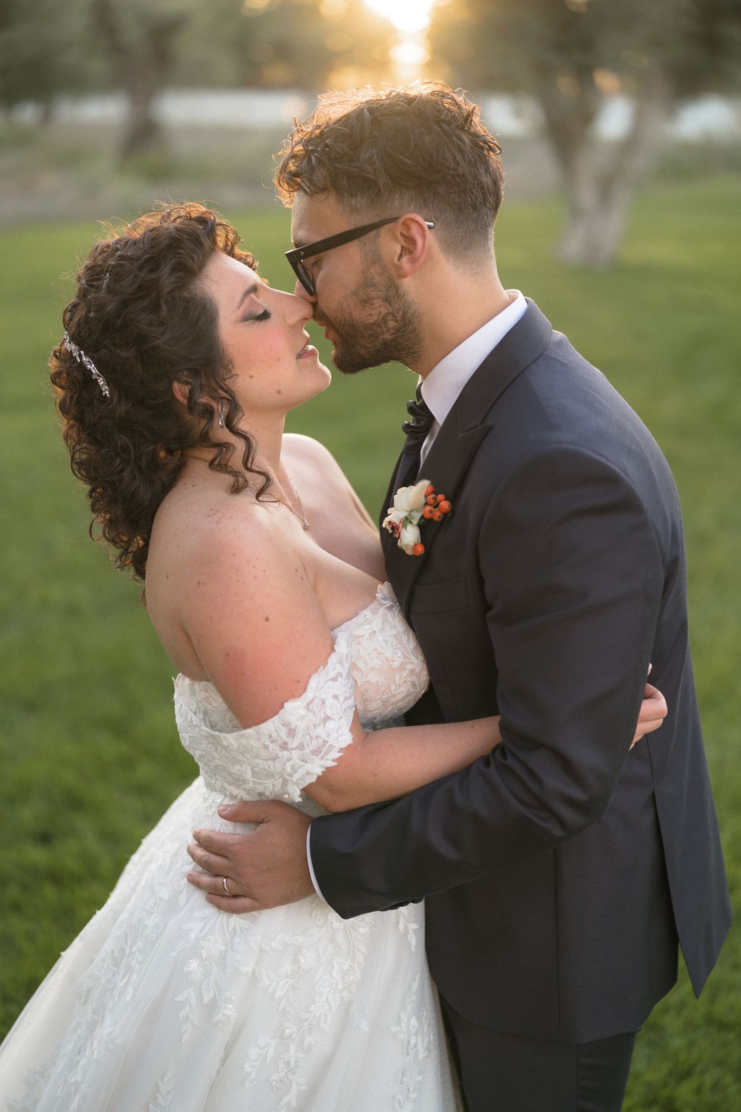Bride and groom sharing a romantic moment at golden hour, embracing in a lush green outdoor setting.