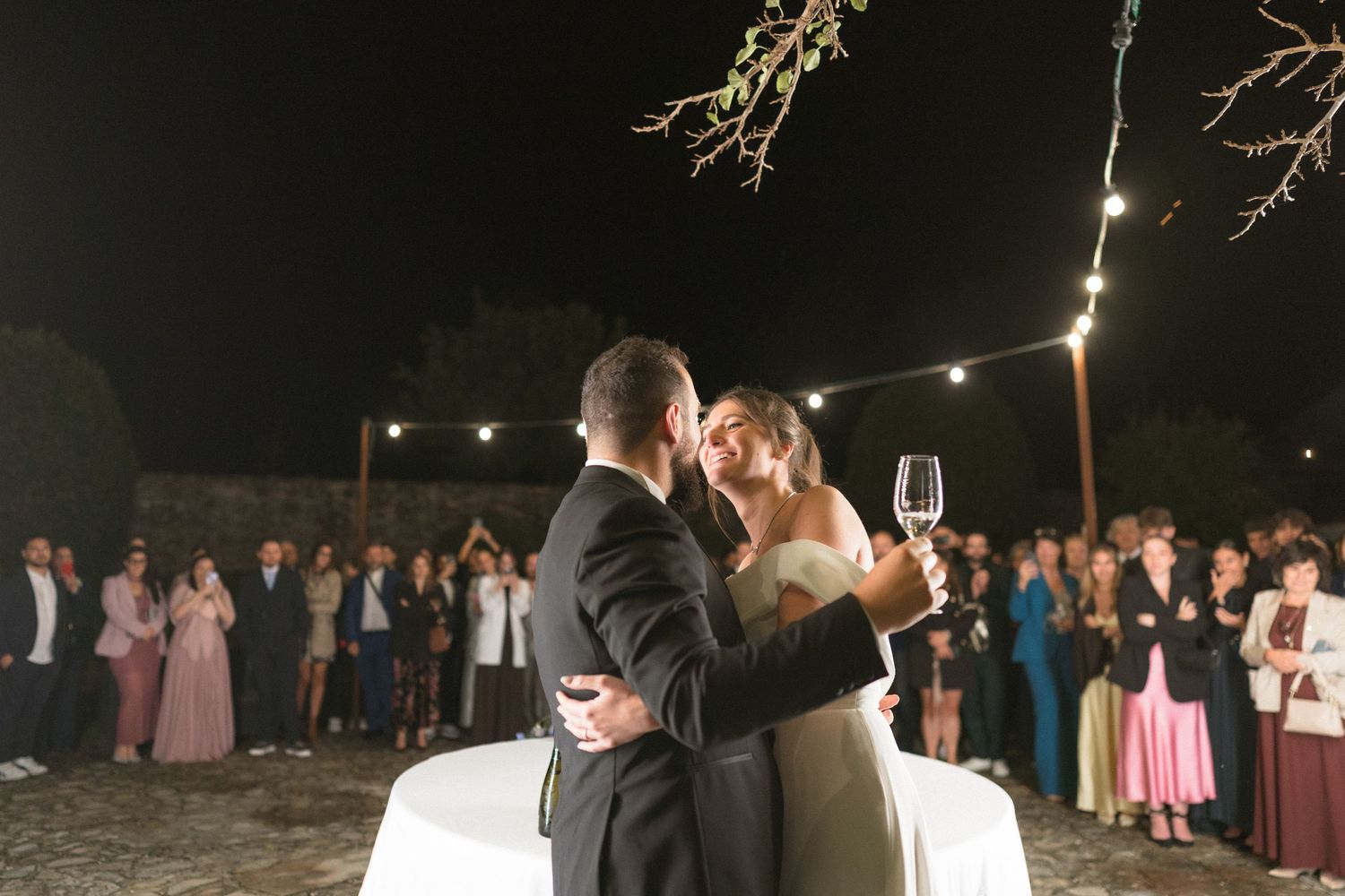 Nighttime outdoor celebration with string lights illuminating a crowd of wedding guests.