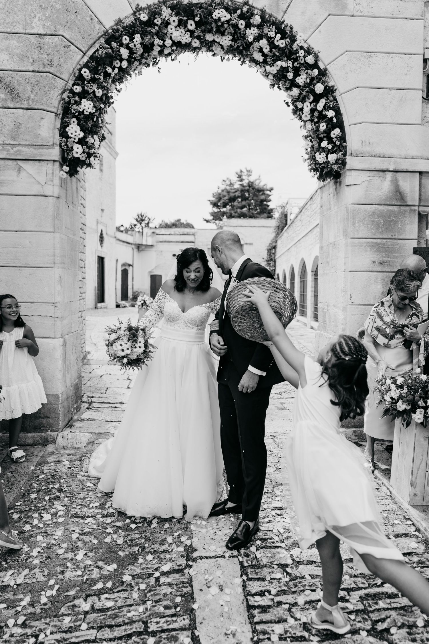 Sequence of wedding photos under a floral arch with flower petals scattered on the ground.