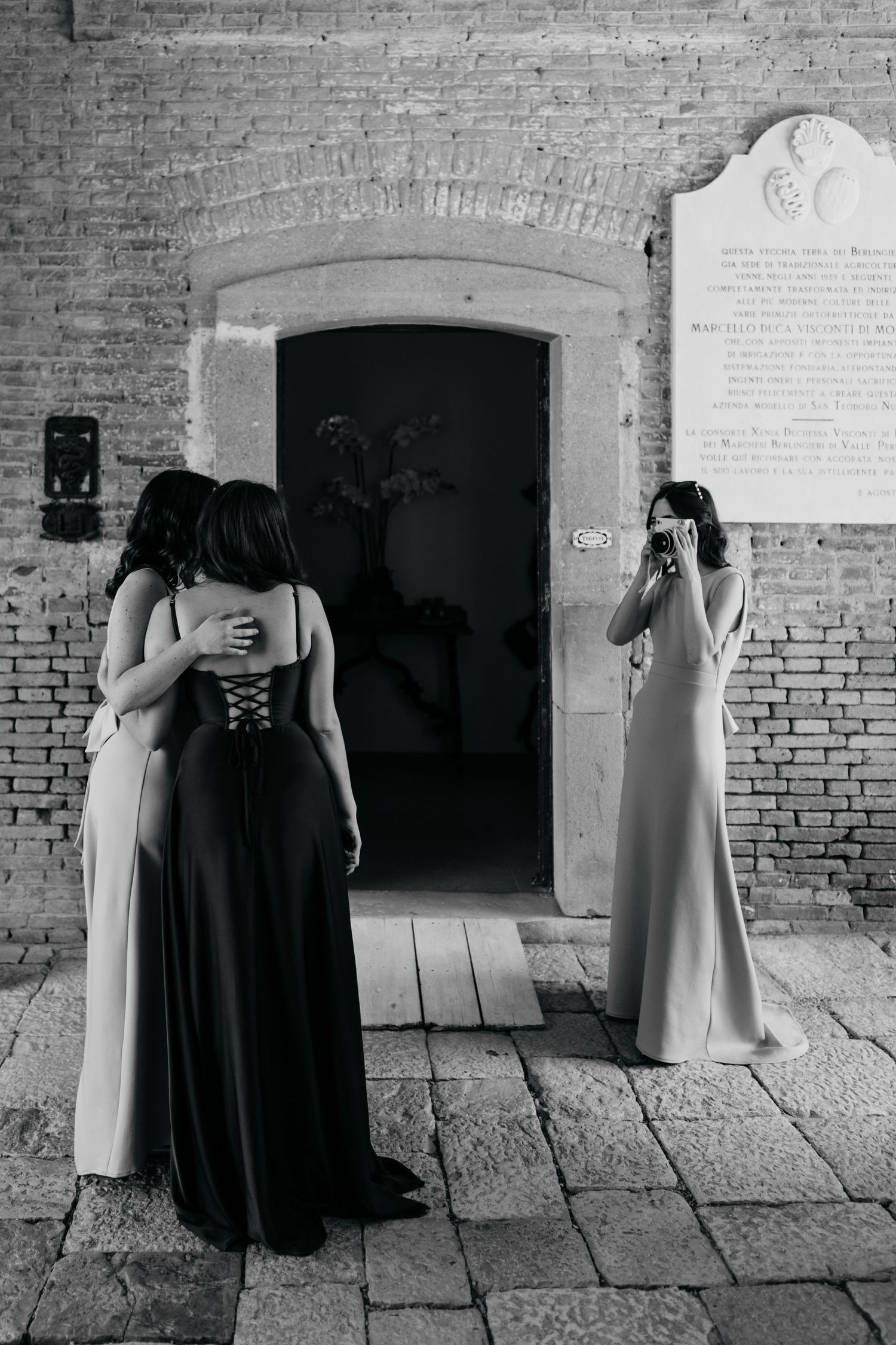 Black and white photo of bridesmaids in dark dresses against brick wall.