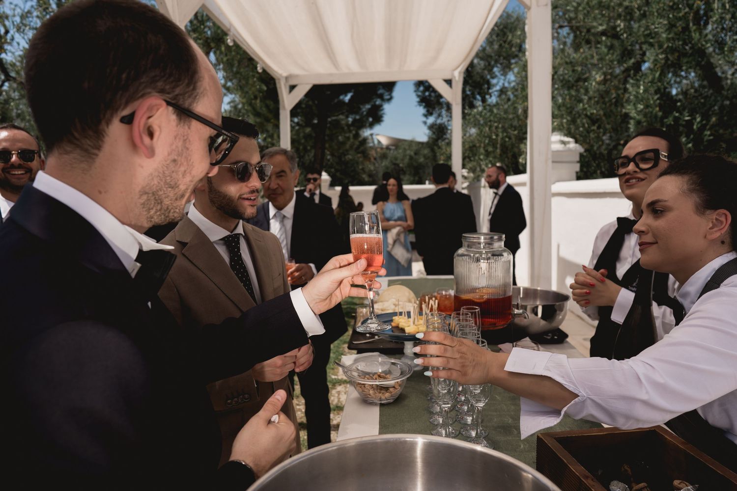 Wedding guests enjoying cocktails at outdoor bar during reception.