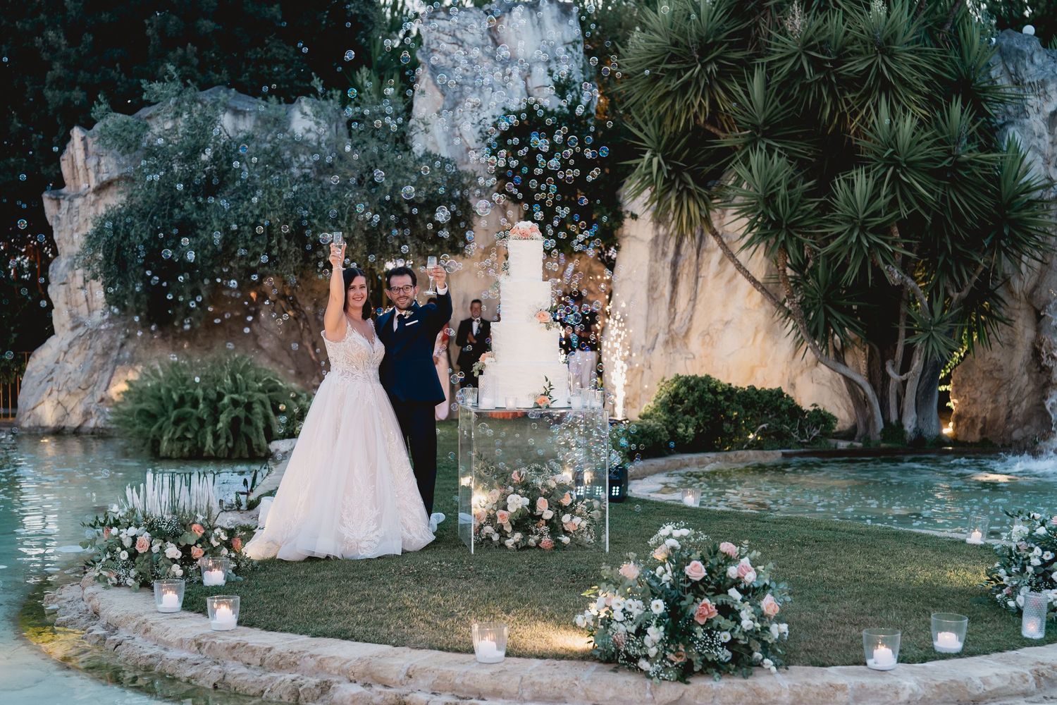 A wedding ceremony scene with floral decorations set against a rocky waterscape and tropical plants.