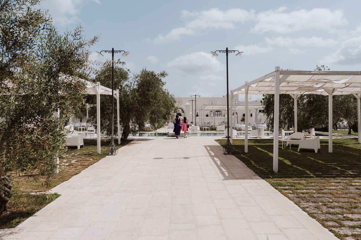 Outdoor wedding venue with white walkway, pergolas and landscaping under blue sky.