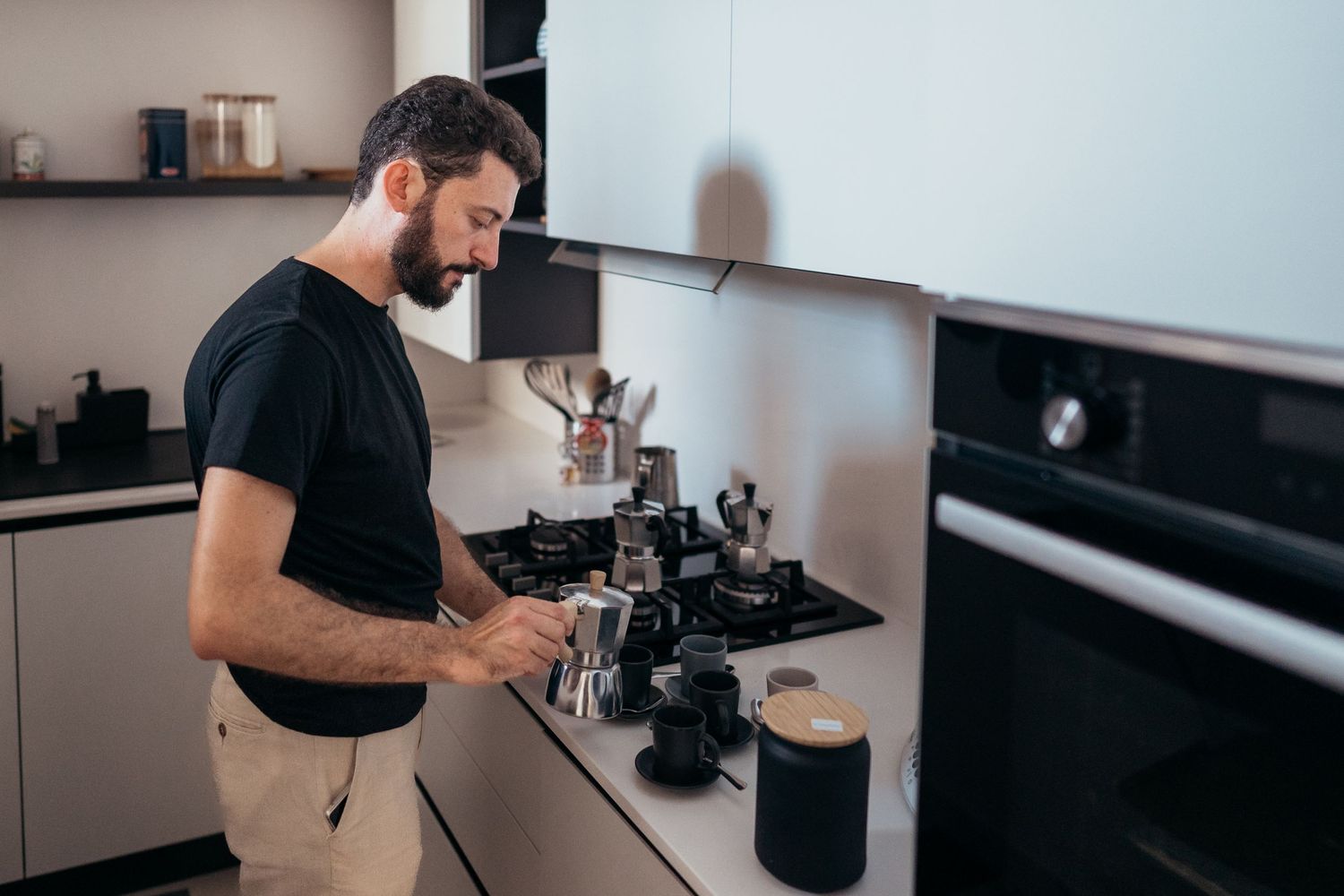 Person in black t-shirt preparing coffee at a modern kitchen counter.