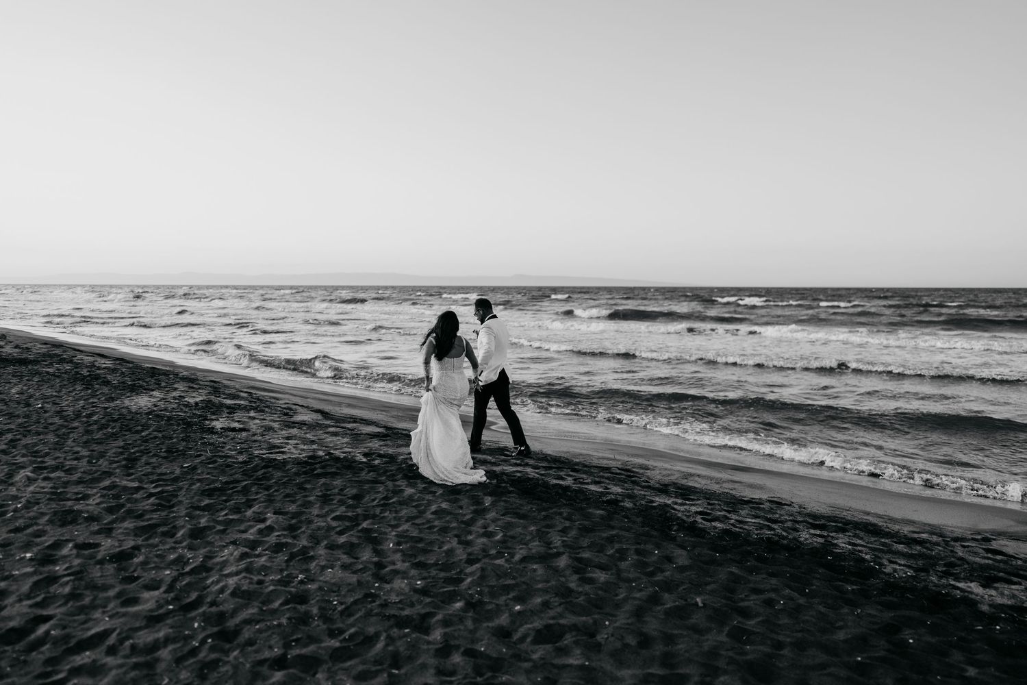 A romantic black and white beach scene with a couple walking along the shoreline at sunset.